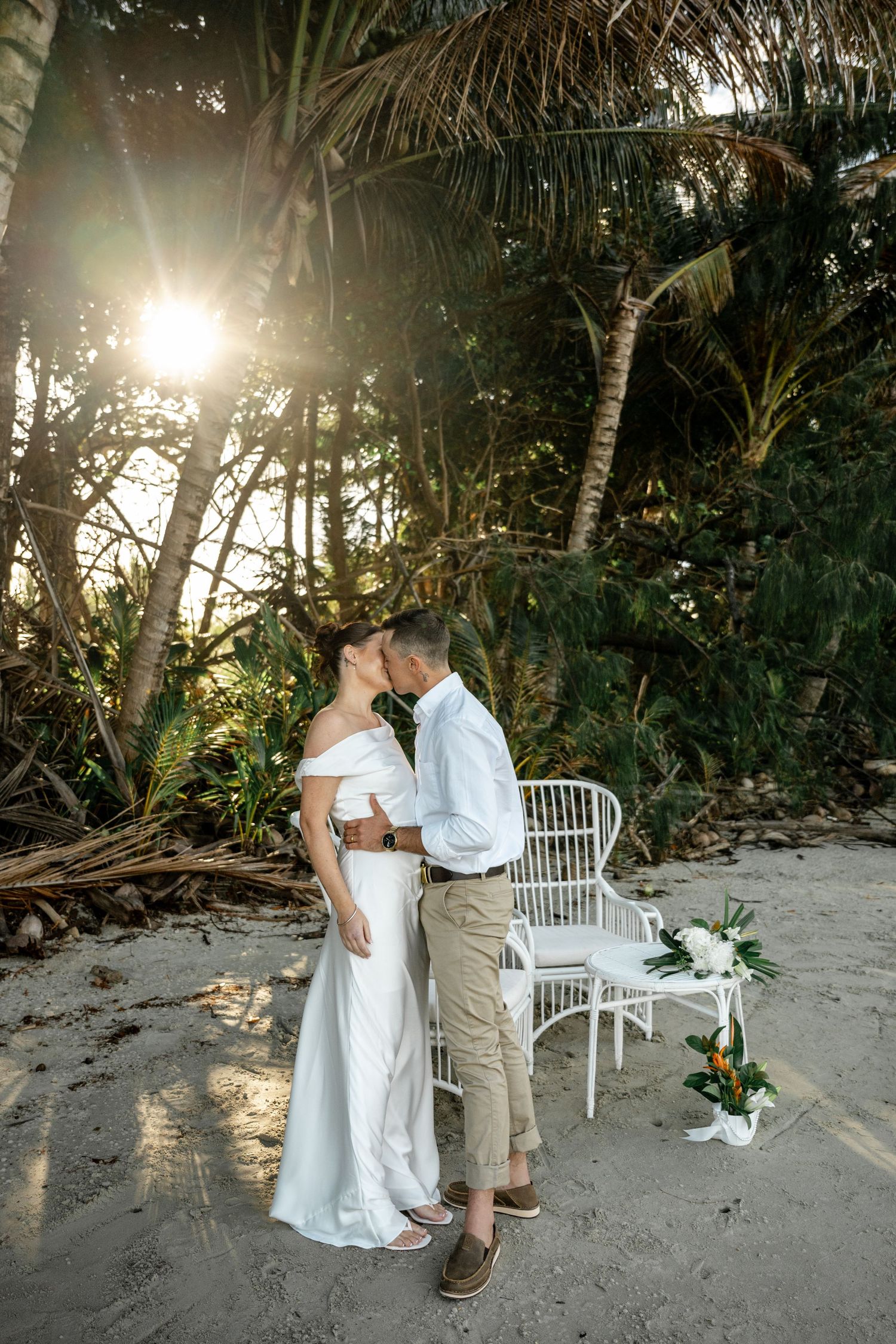 Bride and groom sharing a kiss on a sunlit tropical beach wedding ceremony at Four Mile Beach, Port Douglas.