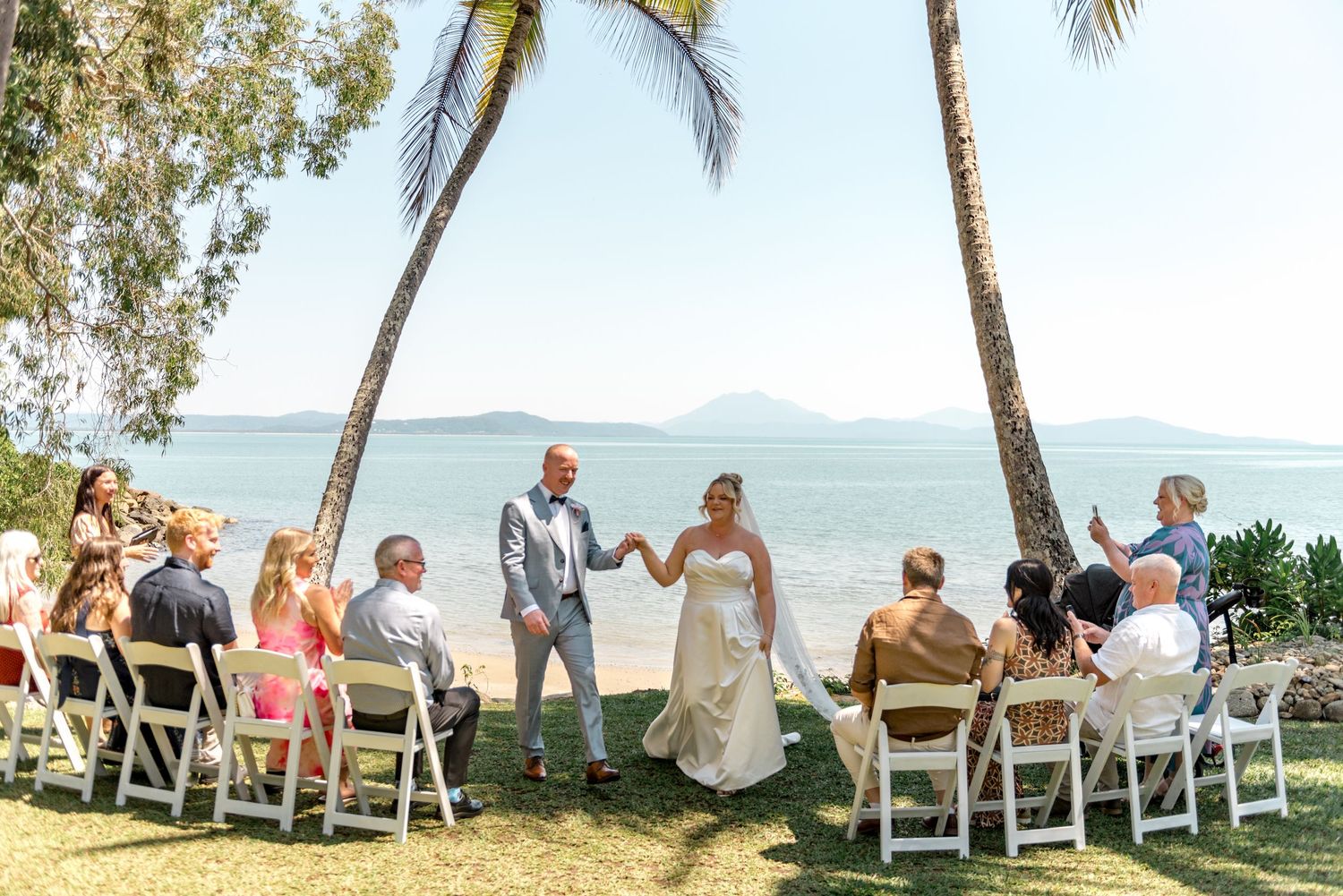 Newlyweds celebrating after beach wedding ceremony under palm trees.