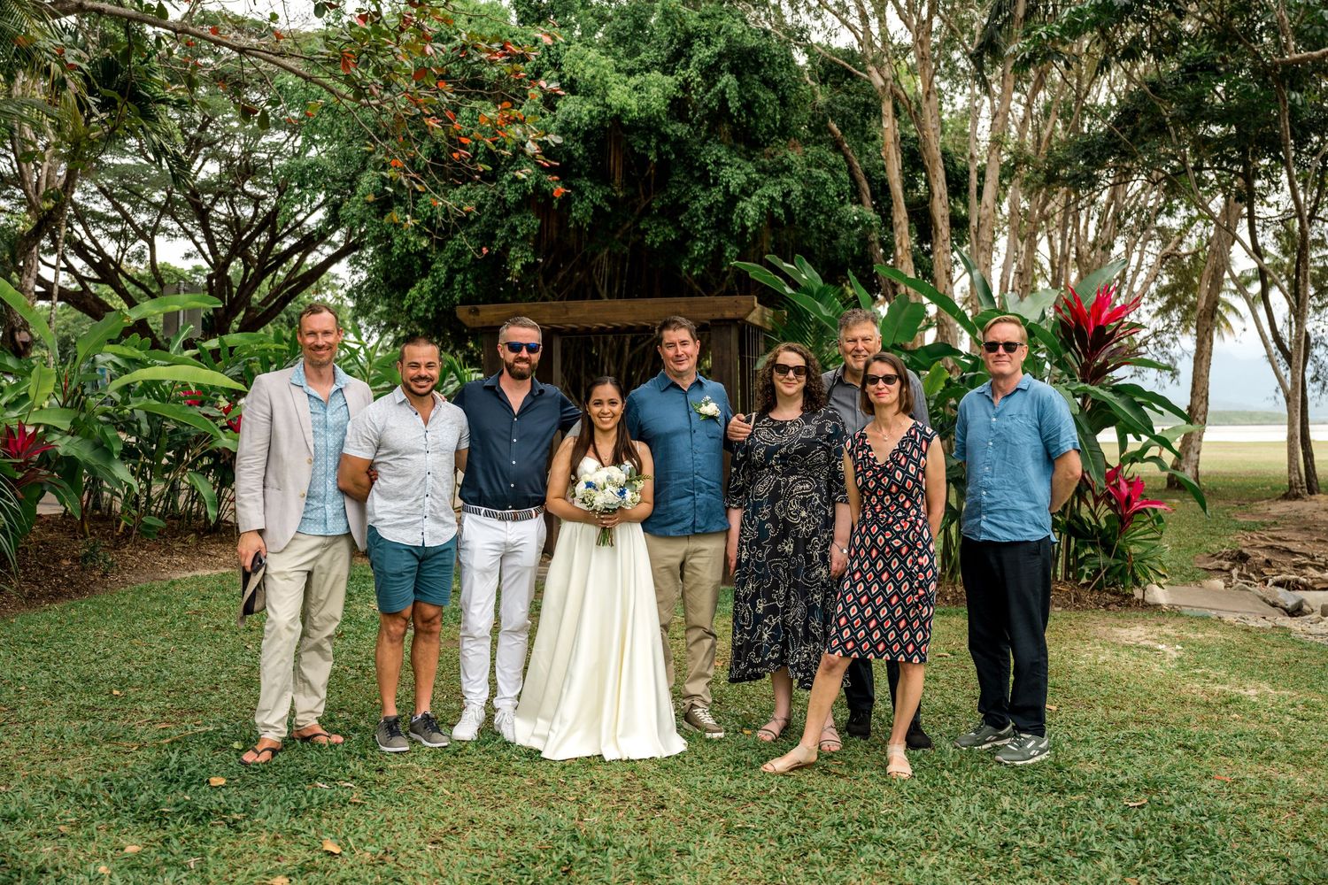 Wedding party group photo with bride and groom surrounded by guests in tropical garden at Little Cove, Port Douglas.