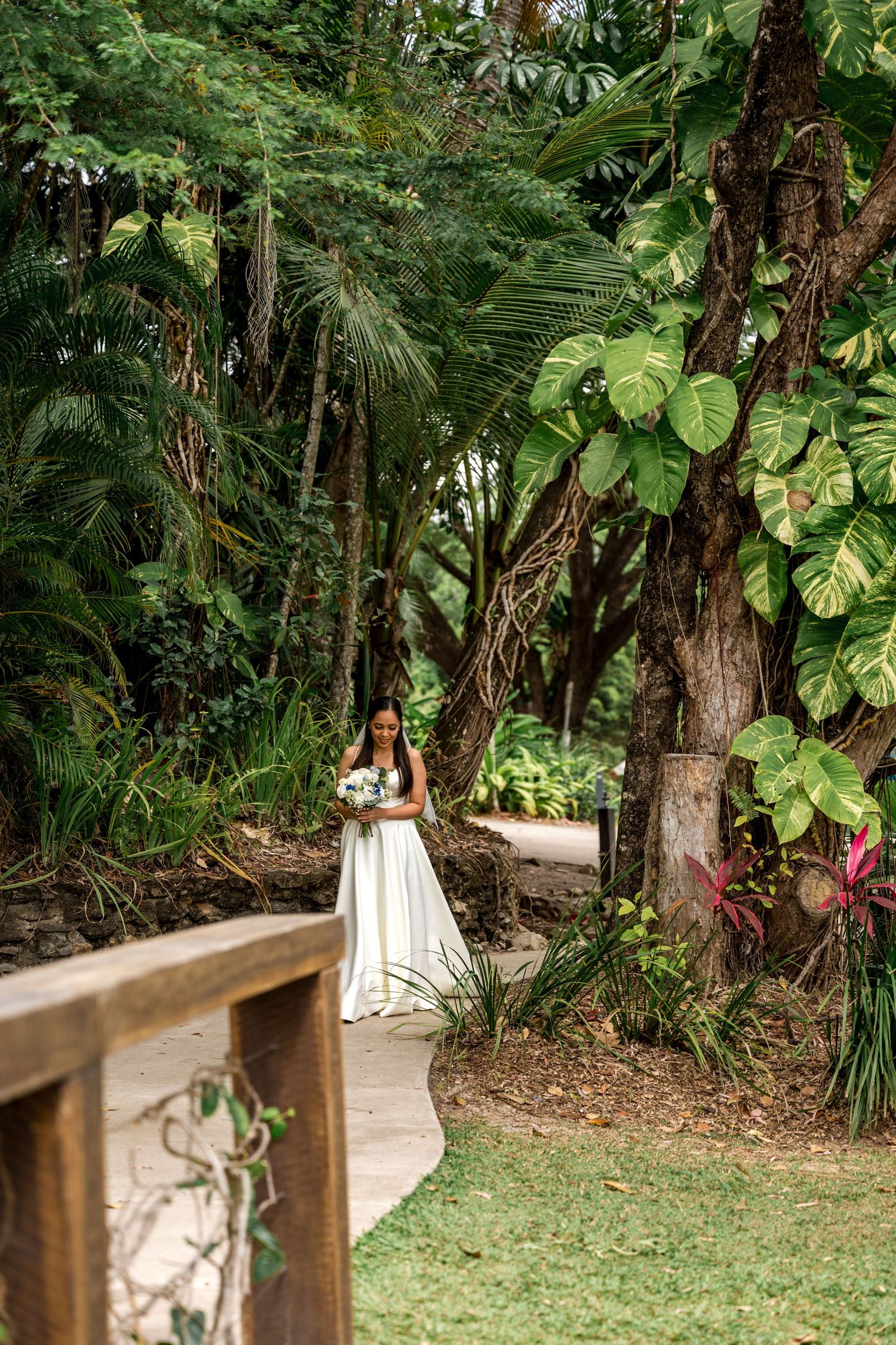 Bride in white satin gown walks along garden path surrounded by tropical foliage at Little Cove, Port Douglas