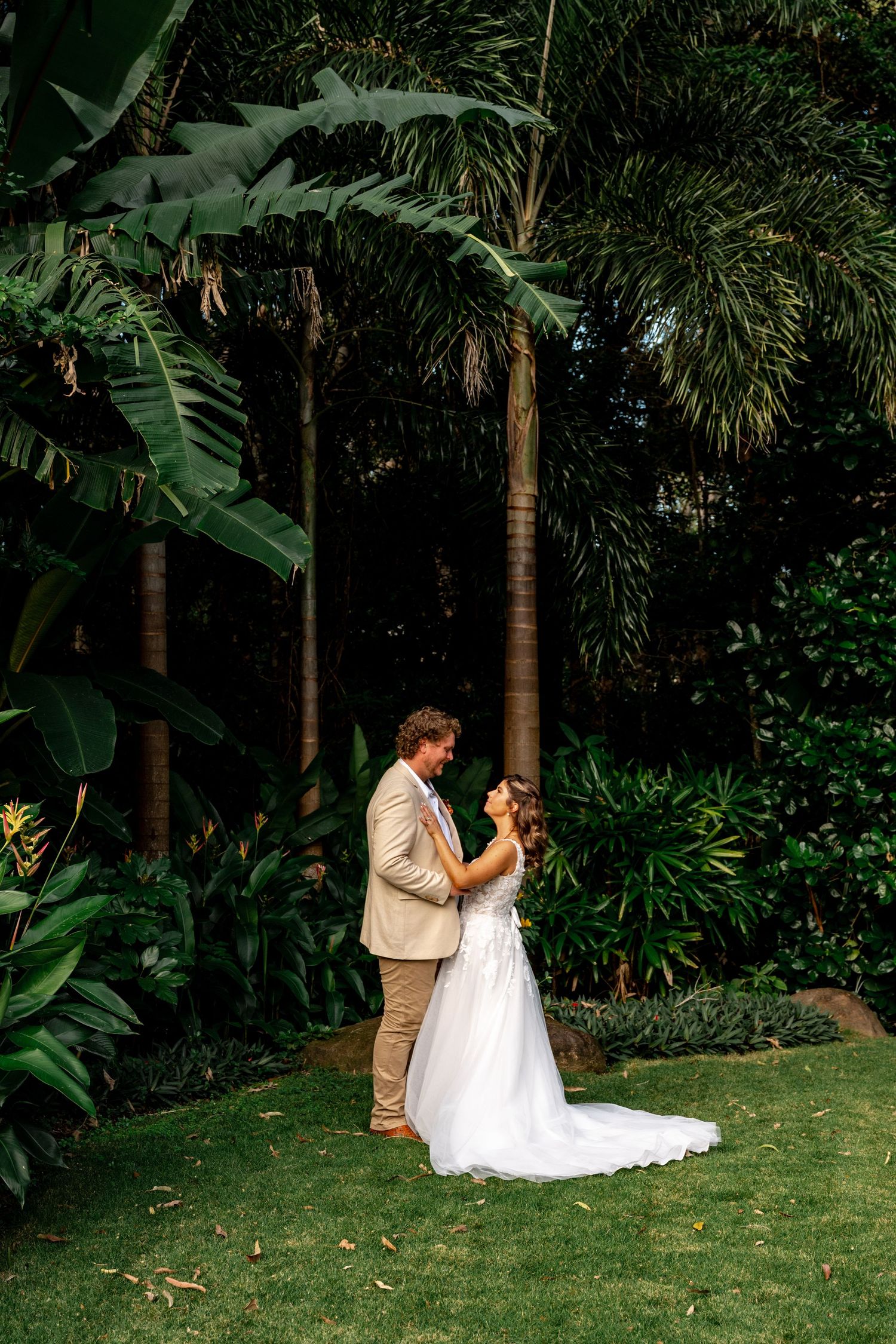 Bride and groom standing together in lush tropical garden with tall palm trees as backdrop at wedding.