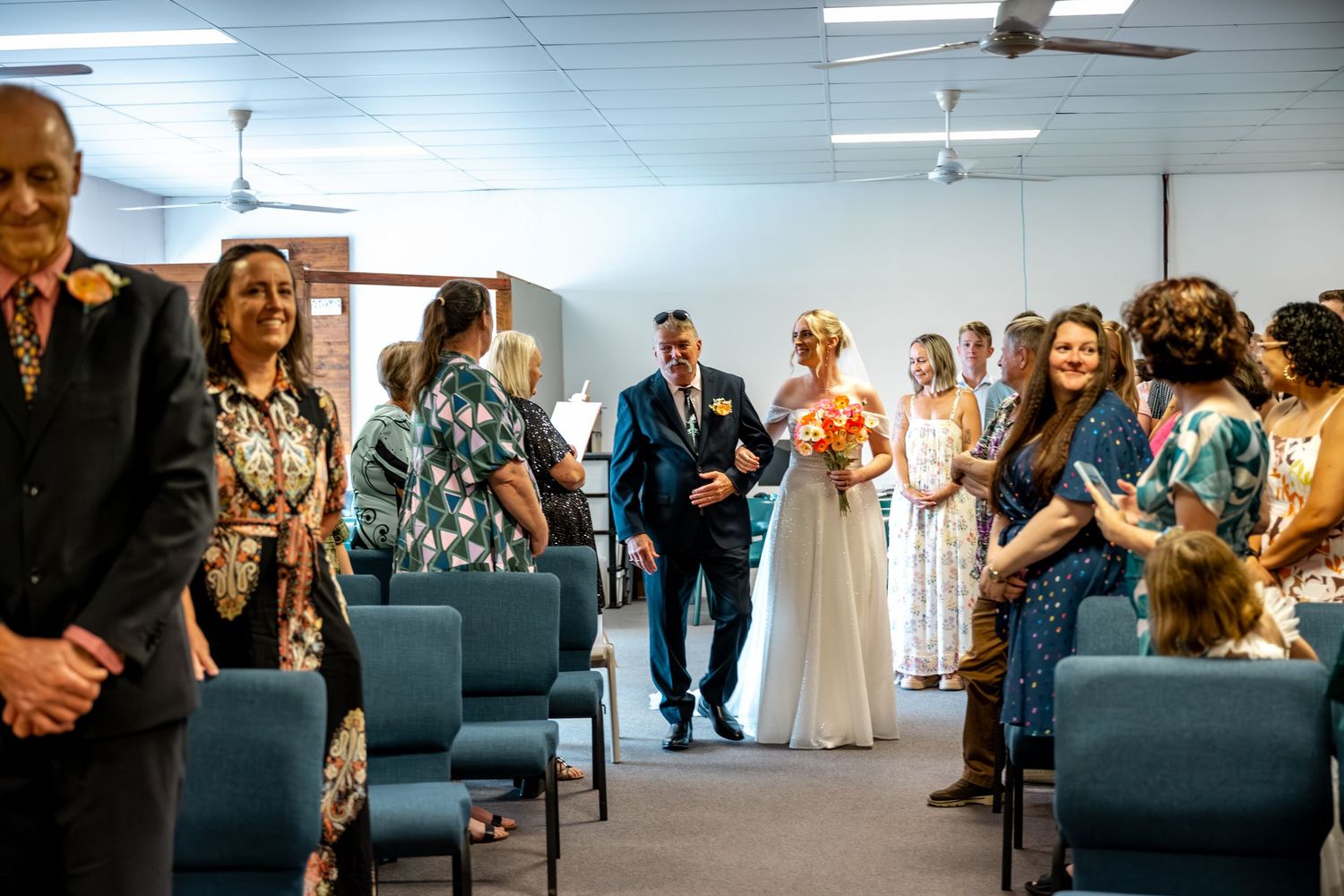 Bride and groom walk back down aisle after wedding ceremony surrounded by smiling guests.