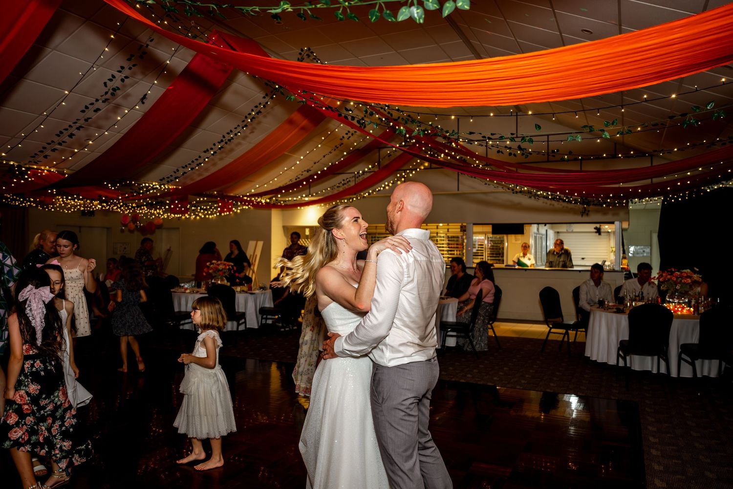 Bride and groom share their first dance under warm orange draped ceiling lights at wedding reception.