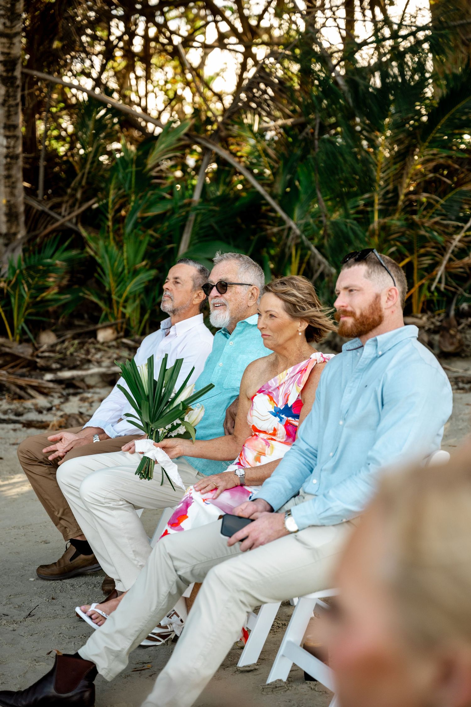Wedding guests seated on white chairs watching a beach ceremony surrounded by lush tropical greenery at Four Mile Beach, Port Douglas.