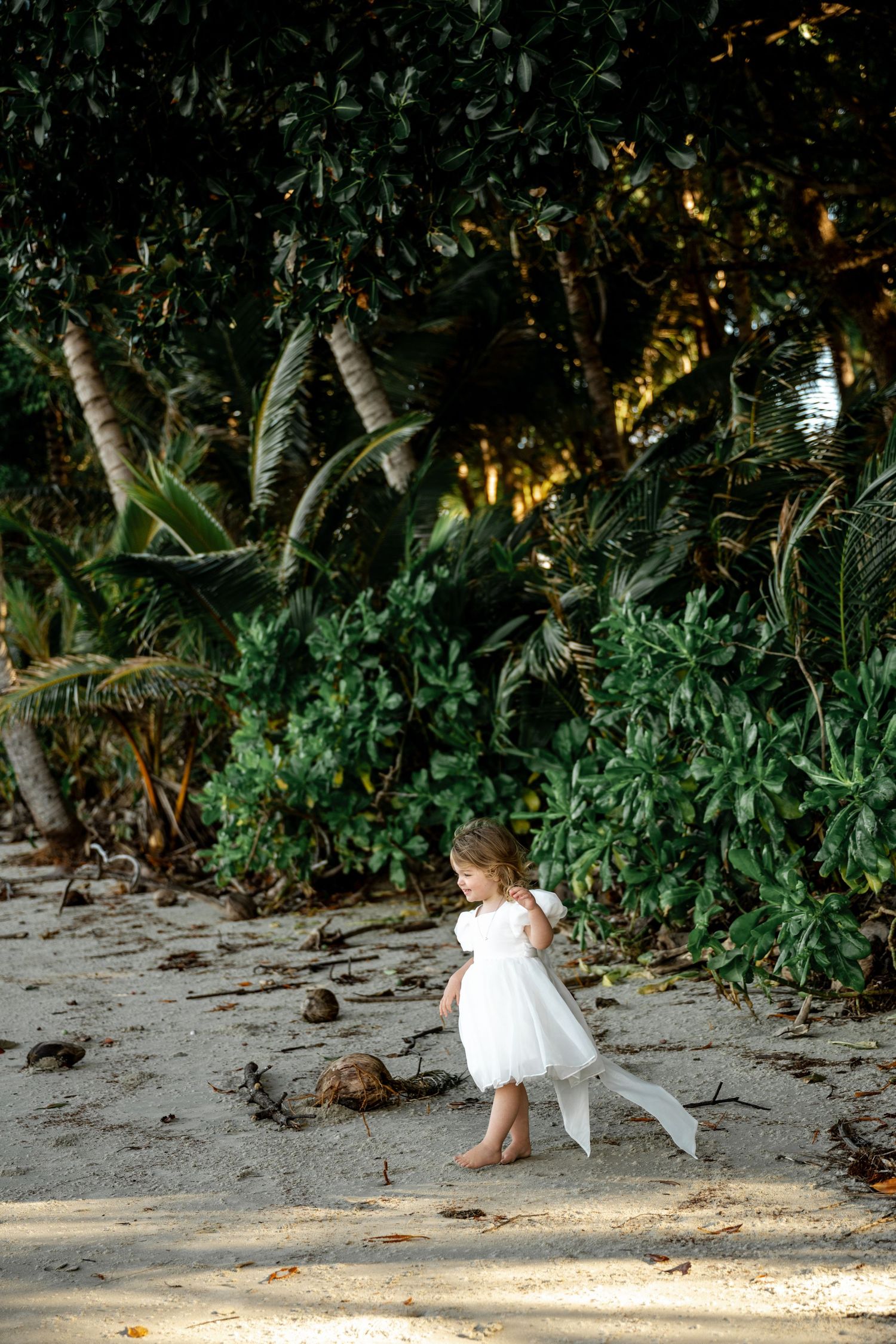 Young flower girl in white dress walking barefoot on sandy tropical beach at Four Mile Beach, Port Douglas.