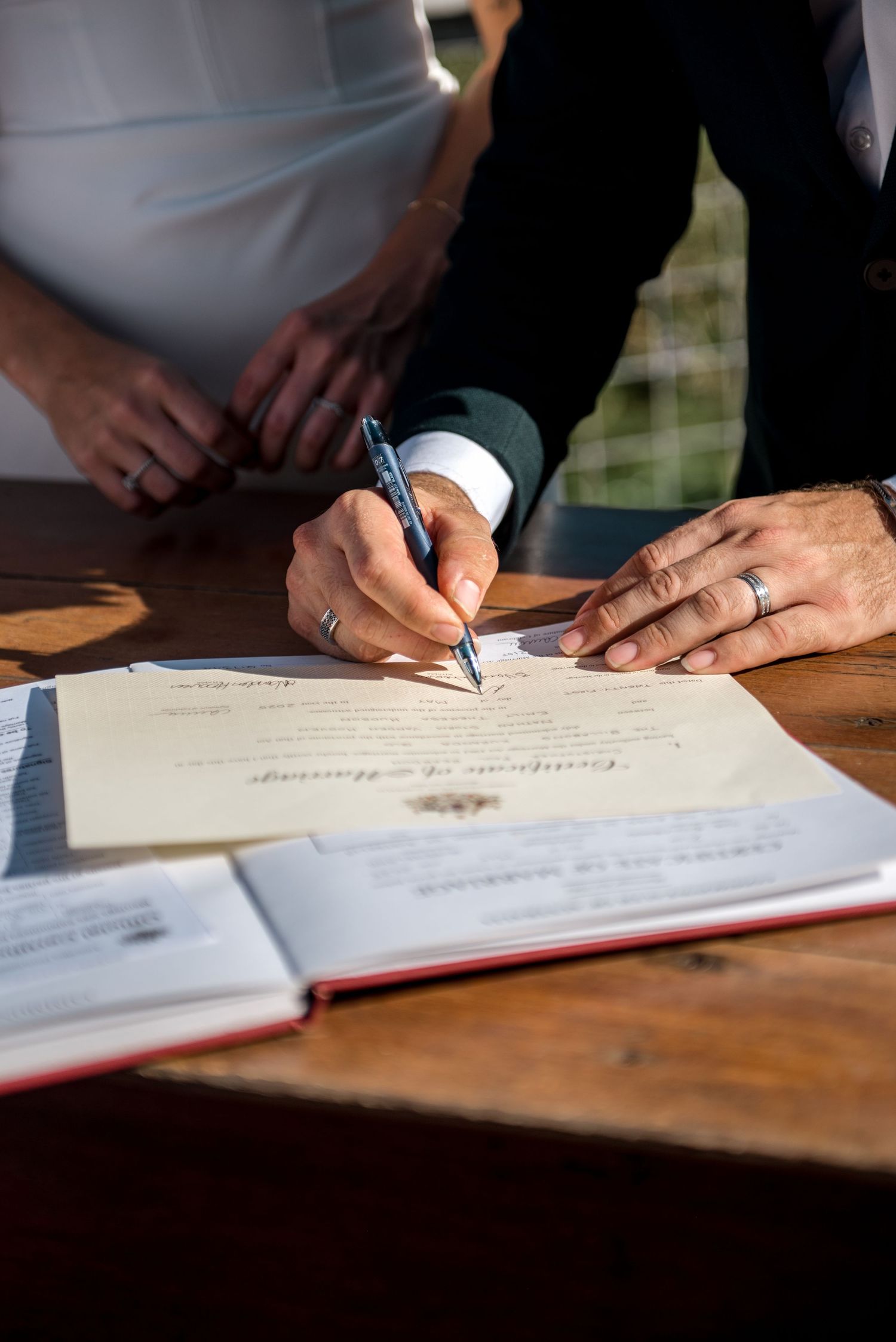 Officiant signing wedding certificate at outdoor ceremony table.