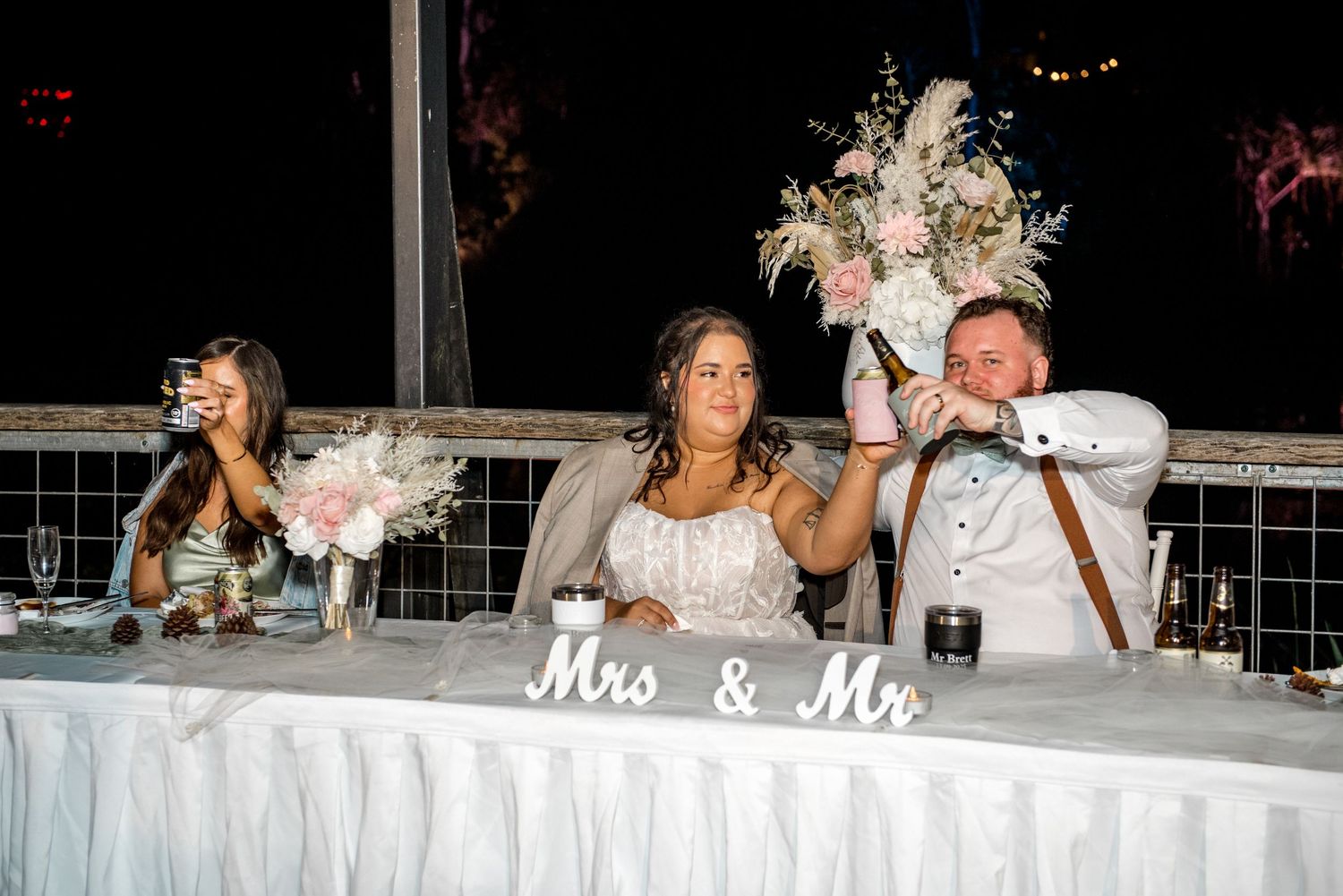 Bride and groom celebrate at head table decorated with Mrs and Mr sign and pink floral bouquets.