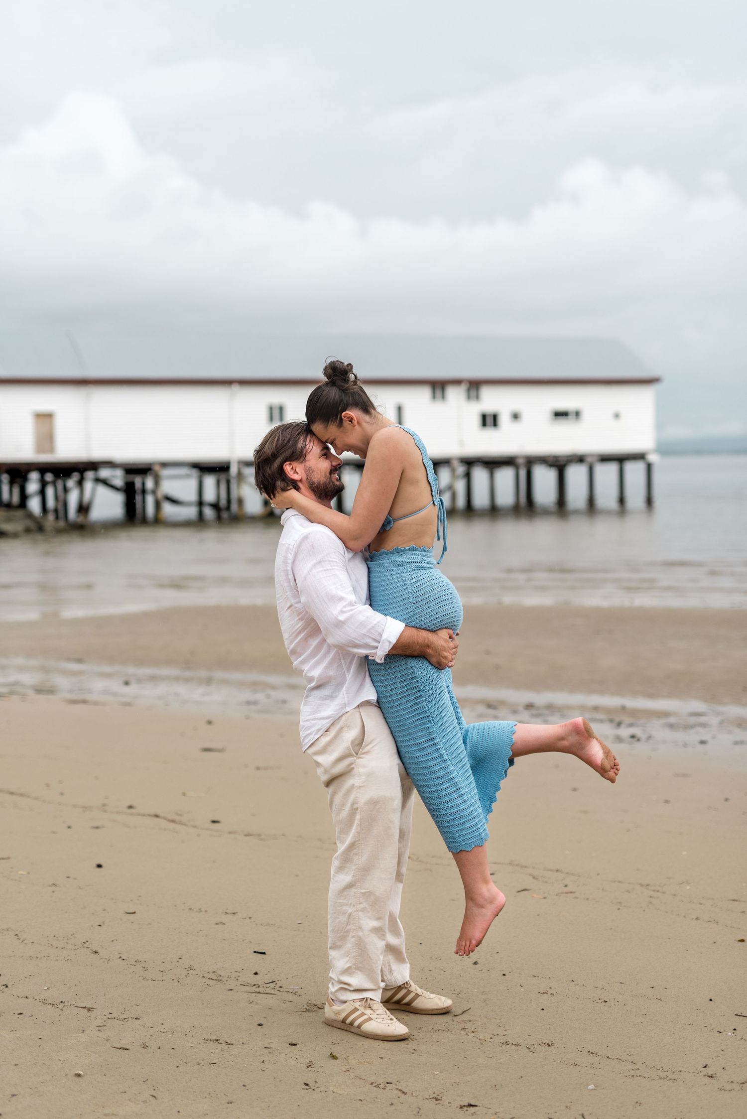 Couple sharing a romantic moment as man lifts woman in blue outfit on a sandy beach.