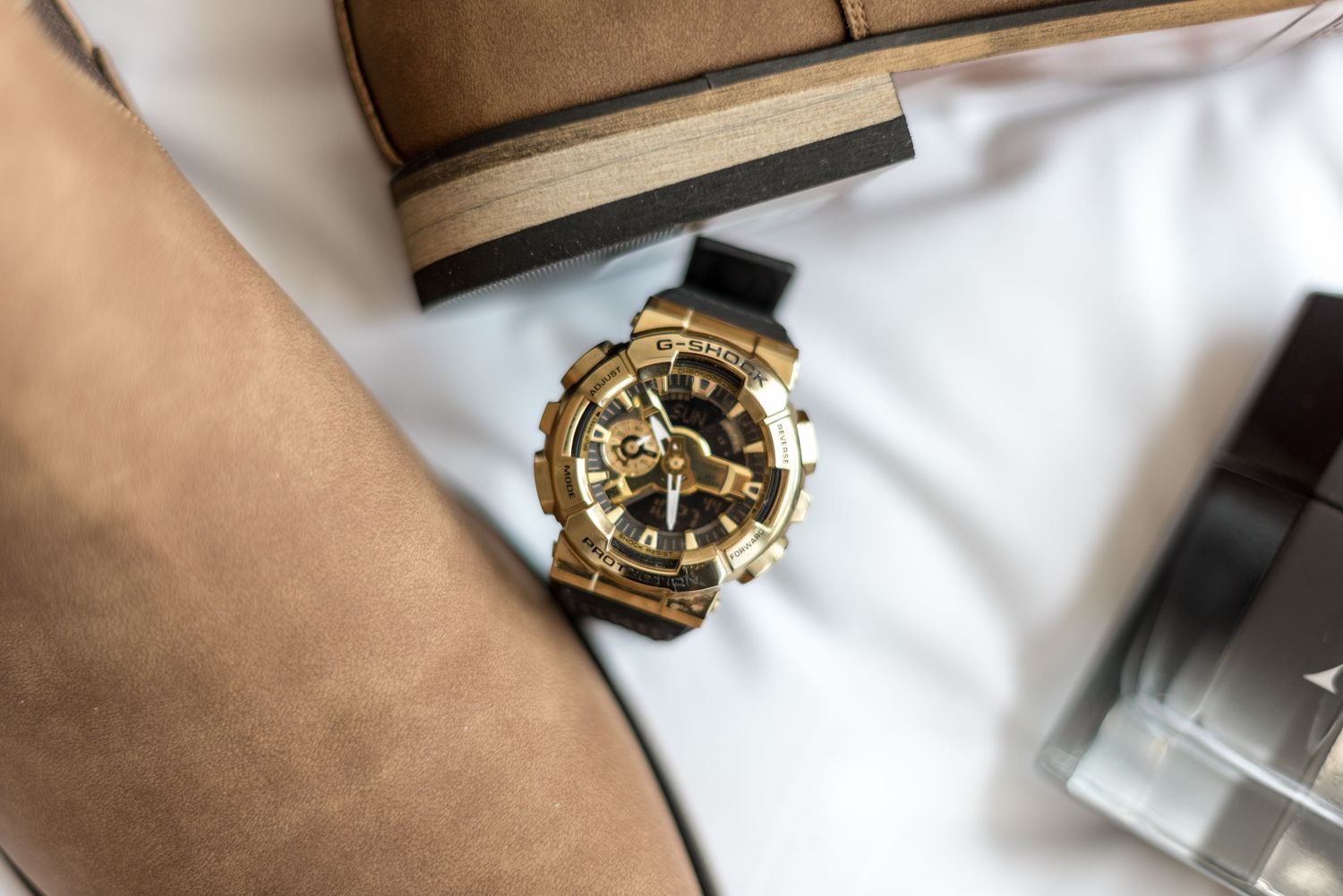 Close-up of a gold and black G-Shock watch on a wrist with wedding accessories in background.