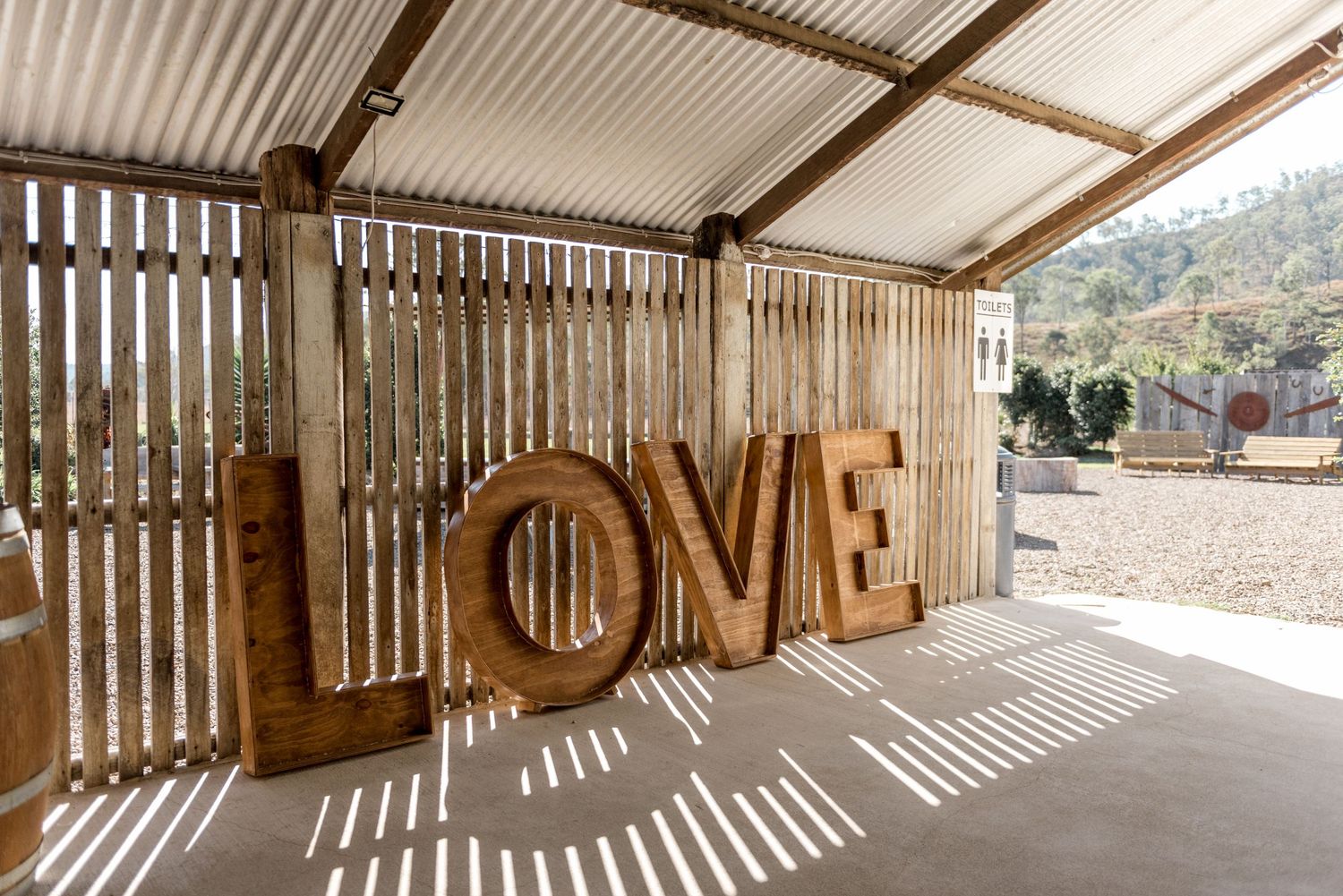 Large wooden LOVE letters display in sunlit rustic barn wedding venue with timber walls.