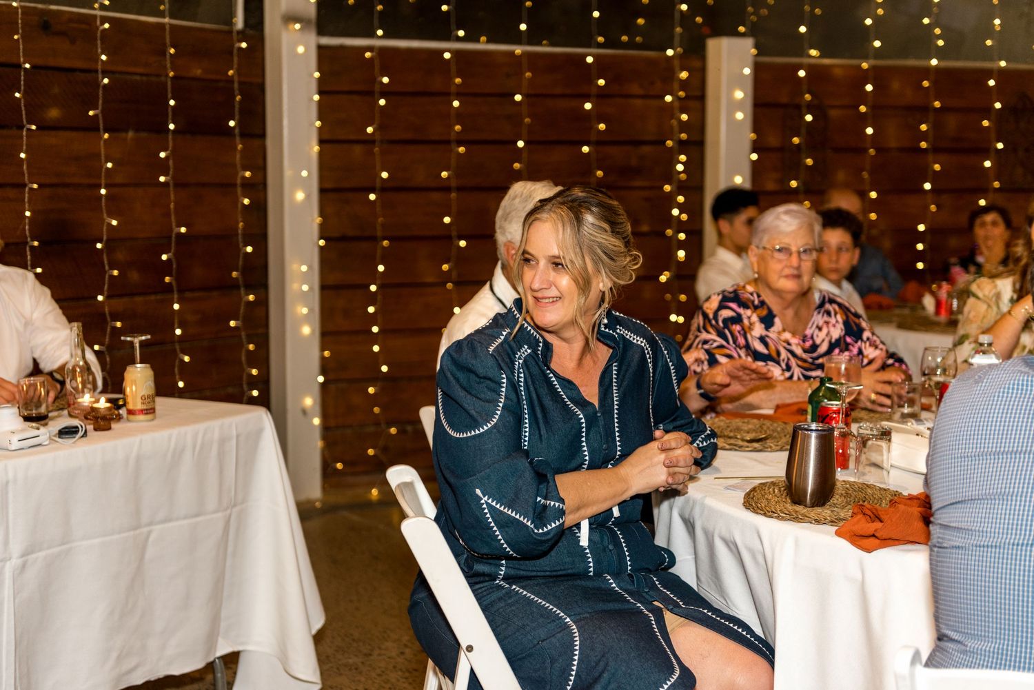 Woman in teal dress smiling at wedding reception with fairy lights backdrop.