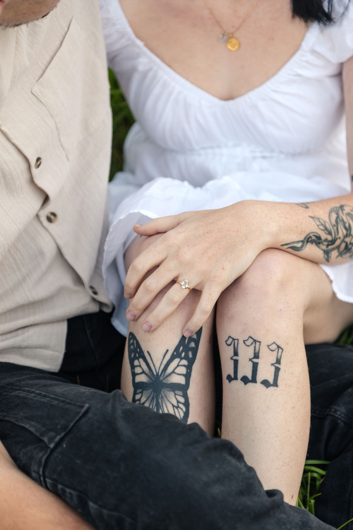 Close-up of couples tattooed legs and hands showing engagement ring, butterfly and 333 tattoos.