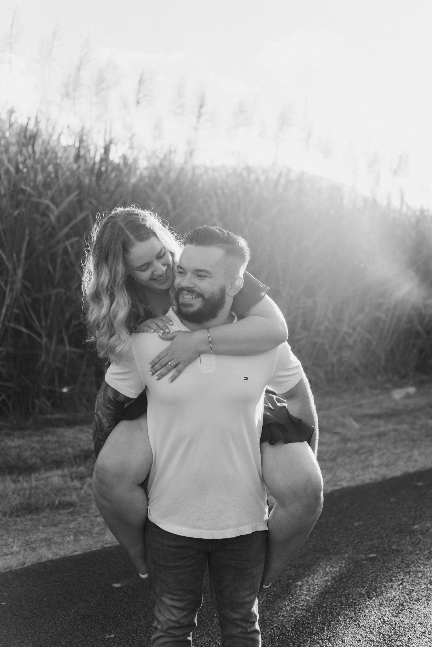 Black and white photo of a couple laughing as a man gives a woman a piggyback ride.