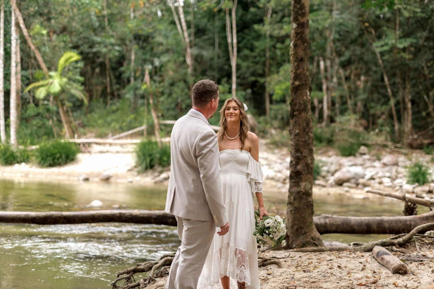 Bride and groom share a romantic moment by a forest creek during their outdoor elopement.