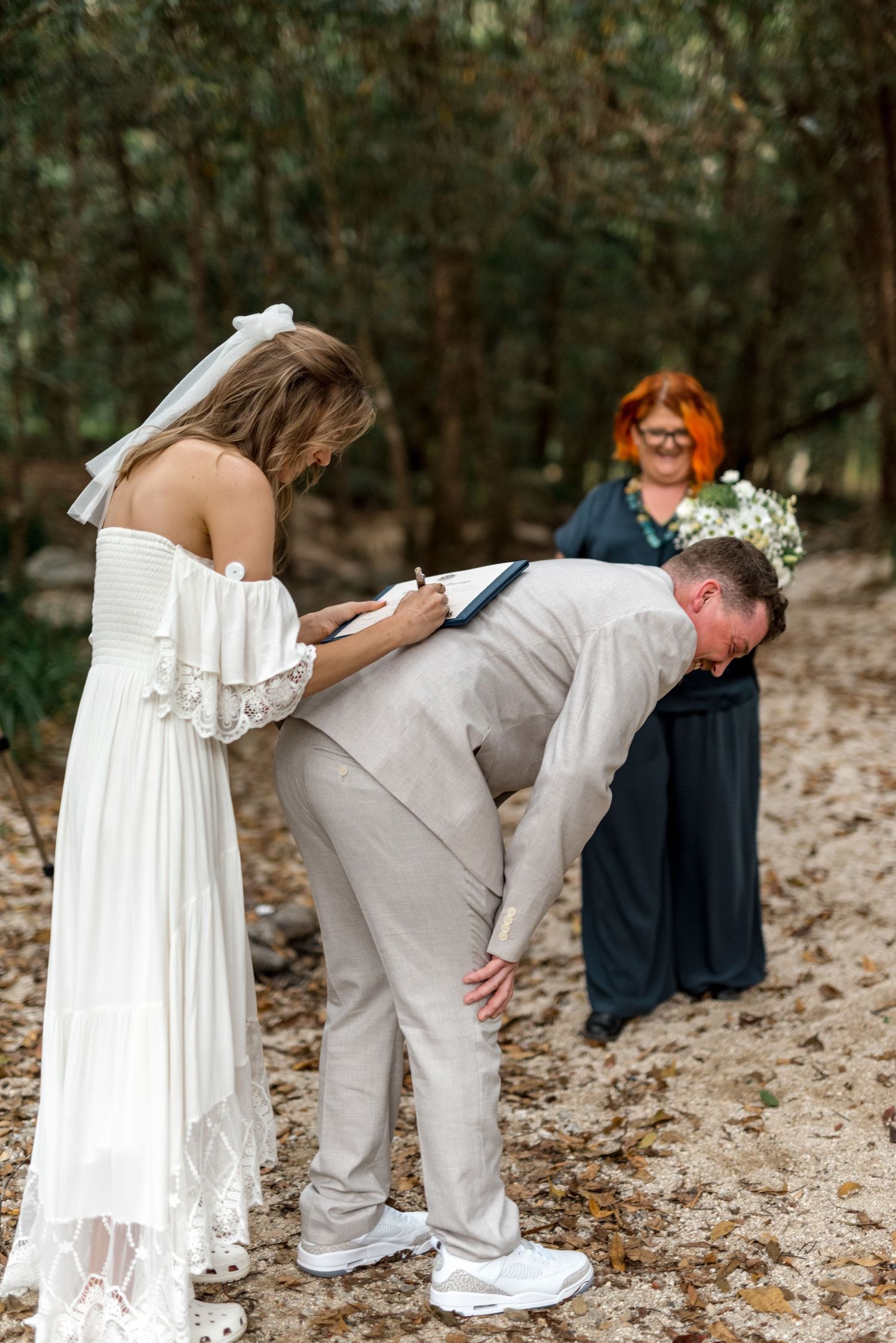 Bride wipes groom's tears during emotional outdoor woodland wedding ceremony with officiant.