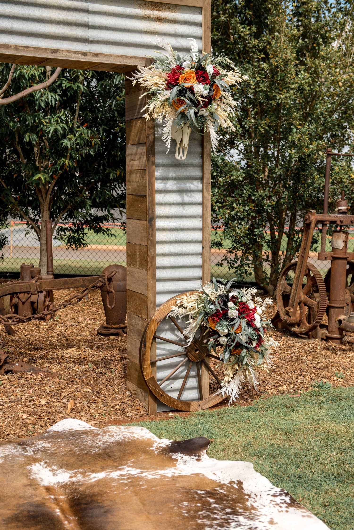 Rustic wedding ceremony arch decorated with dried and fresh floral arrangements and wagon wheel.