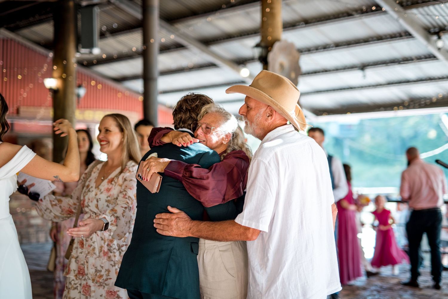 Wedding guests embrace and dance joyfully under a covered outdoor reception venue with festive atmosphere.