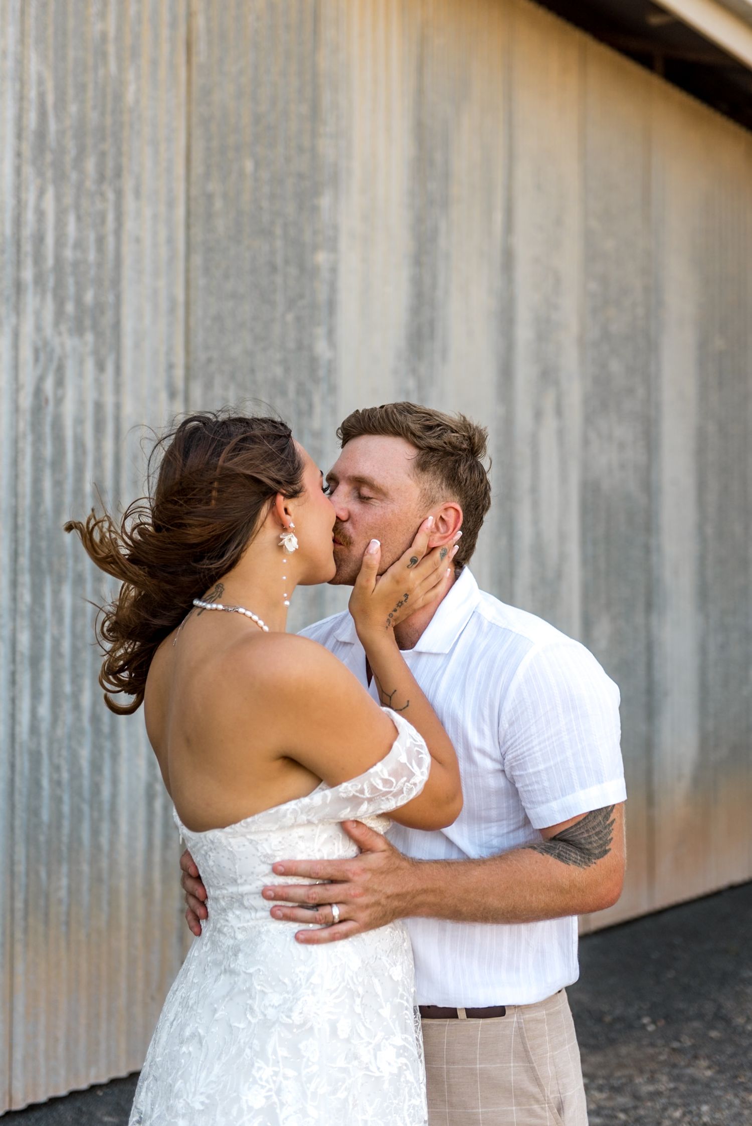Bride and groom share a passionate kiss against a weathered corrugated metal backdrop on their wedding day.