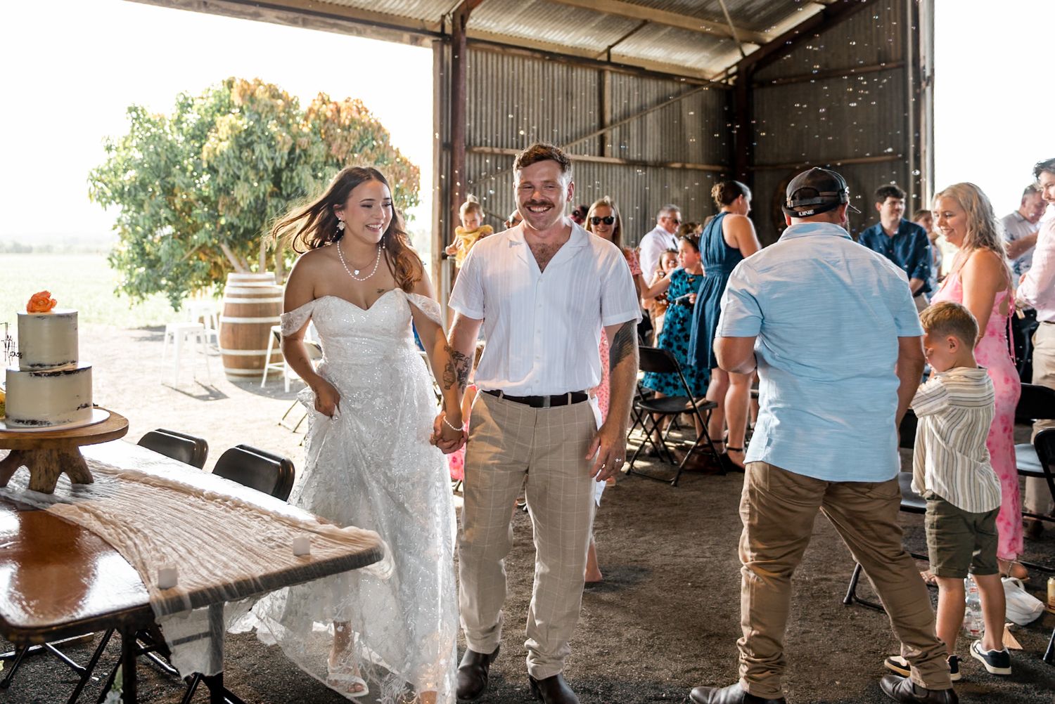 Smiling bride and groom hold hands while entering their rustic barn wedding reception.