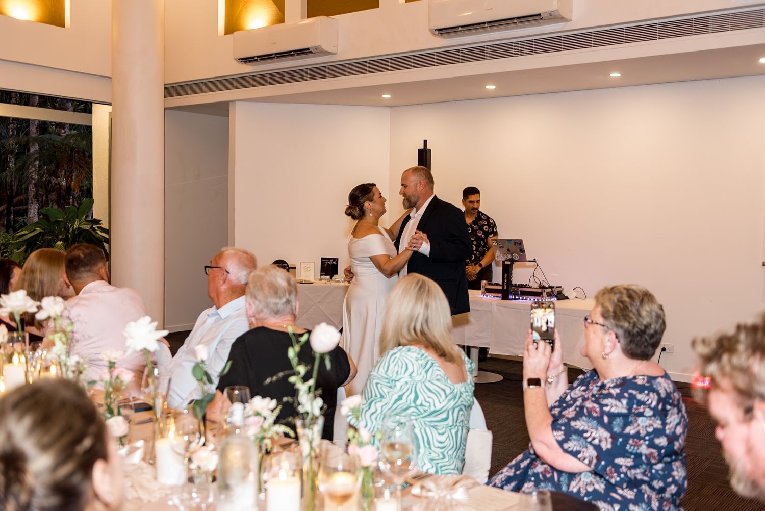 Bride and groom share first dance at elegant wedding reception while guests watch from decorated tables.