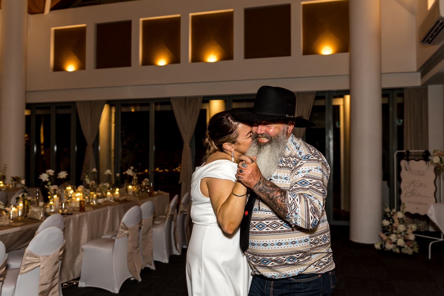 Couple sharing first dance at wedding reception in elegant venue with warm lighting and decorated tables.