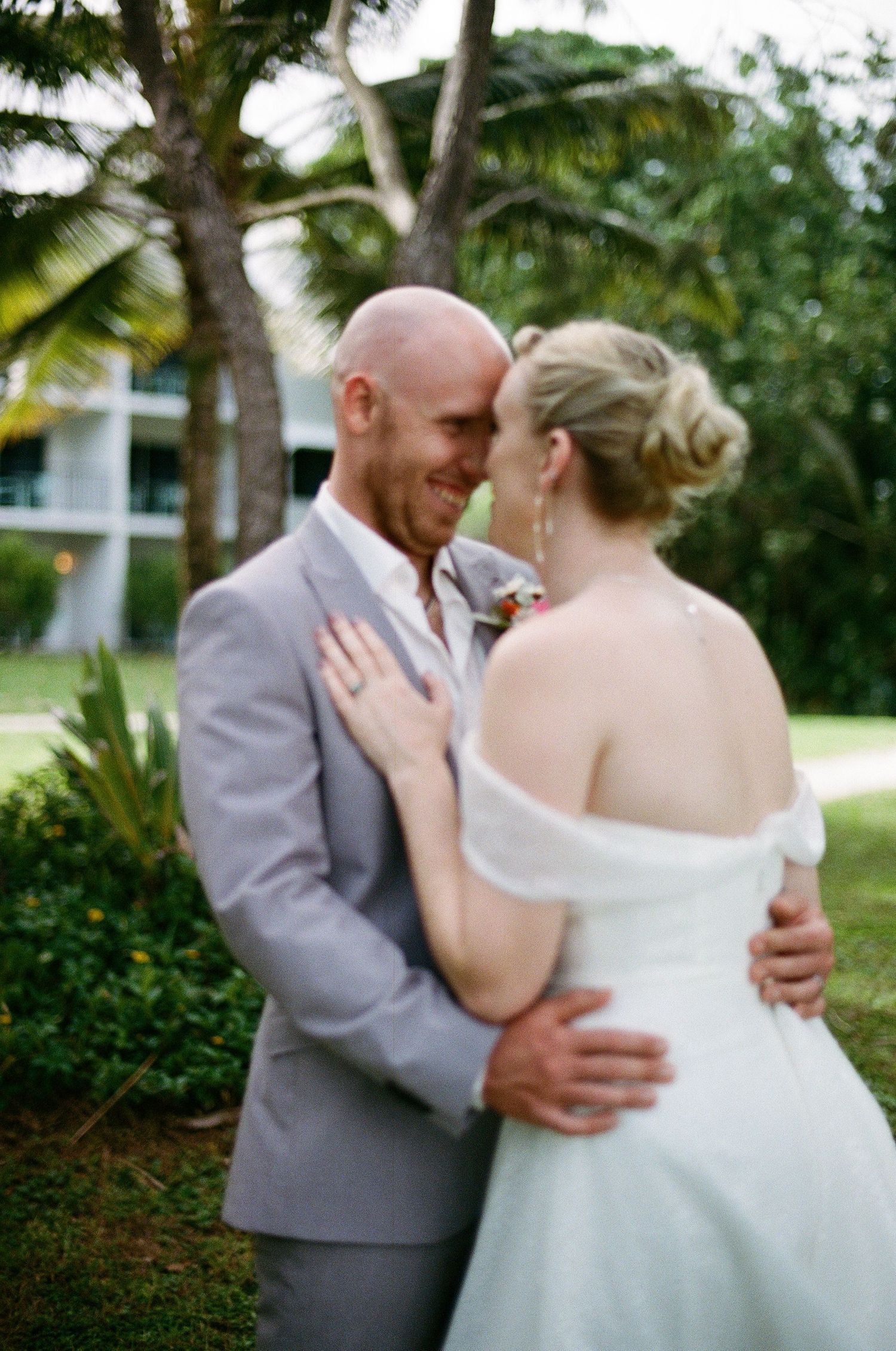 Bride and groom share a romantic moment outdoors surrounded by lush tropical palm trees at their destination wedding.