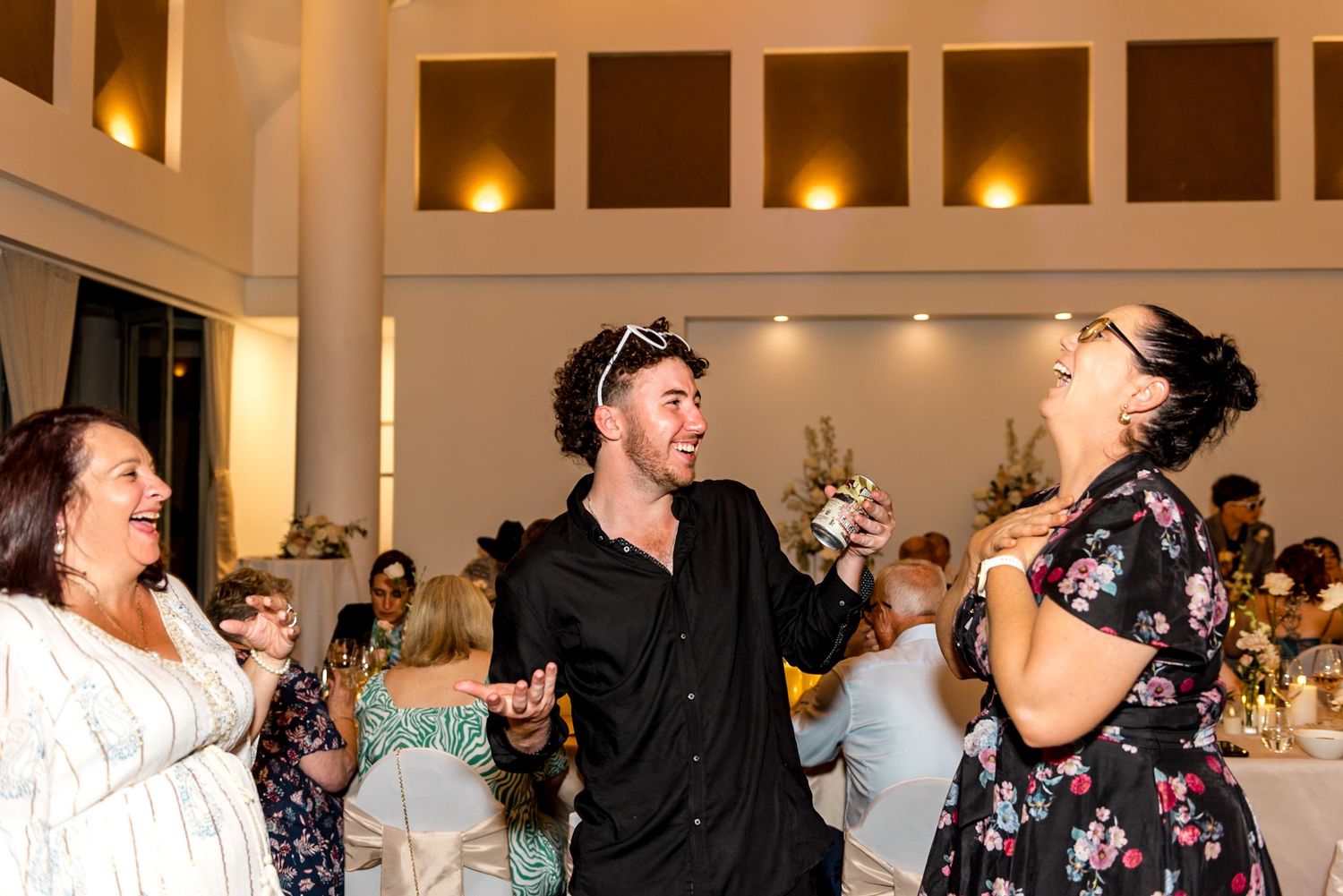 Three guests laughing and dancing together at lively wedding reception celebration.