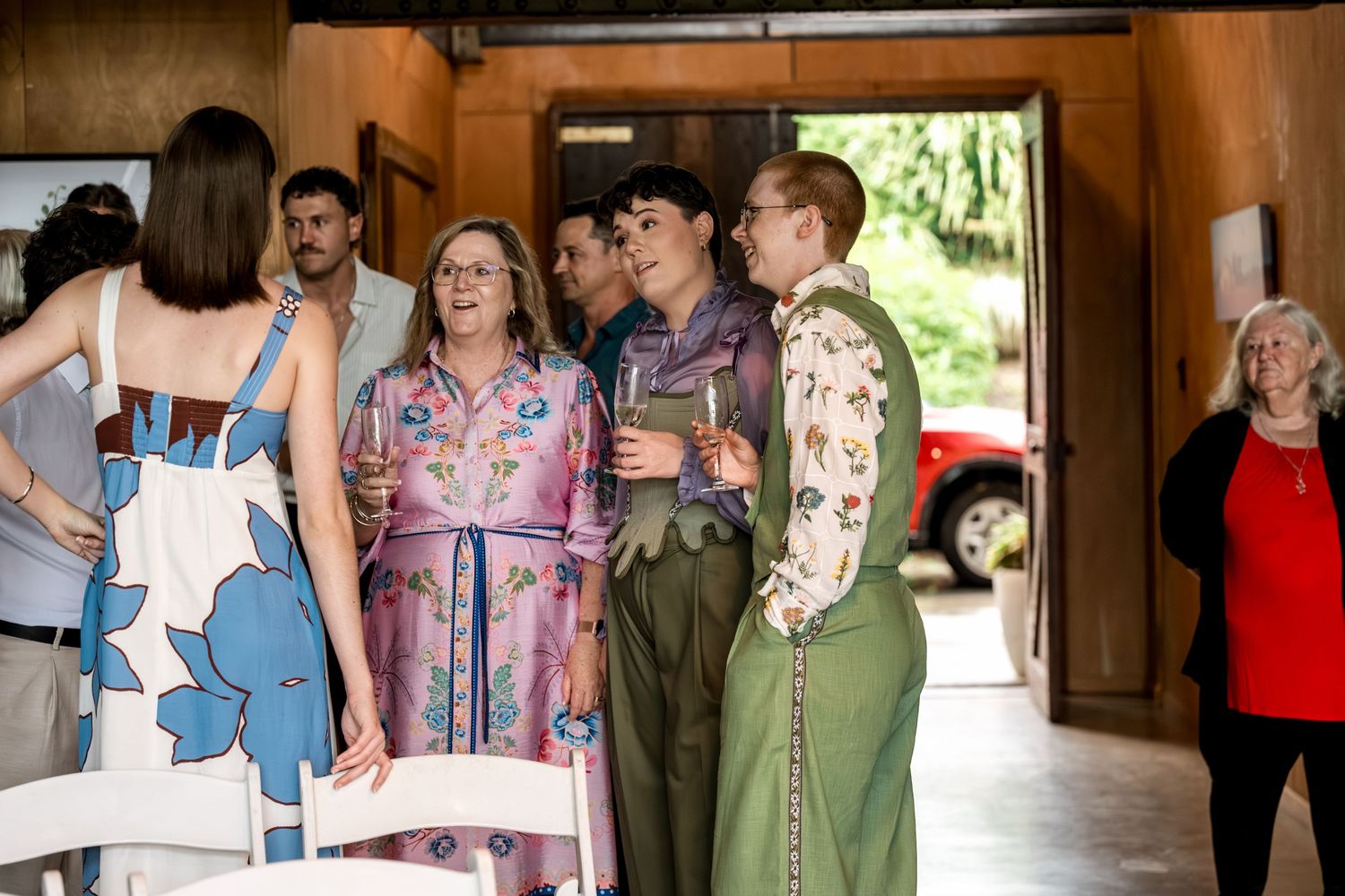 Elegantly dressed wedding guests socializing in a rustic venue doorway.