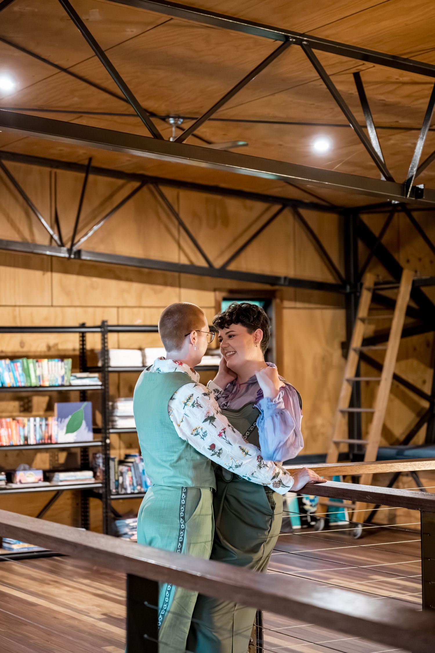 Two women laugh and dance together on a wooden deck inside a rustic barn venue.