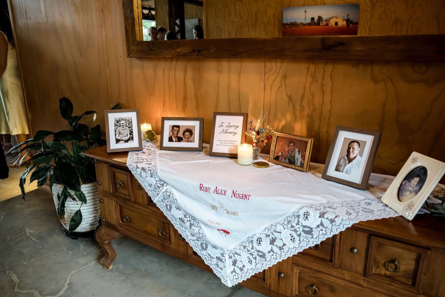 Memorial table with framed photos, candles, and lace tablecloth displaying cherished family memories.
