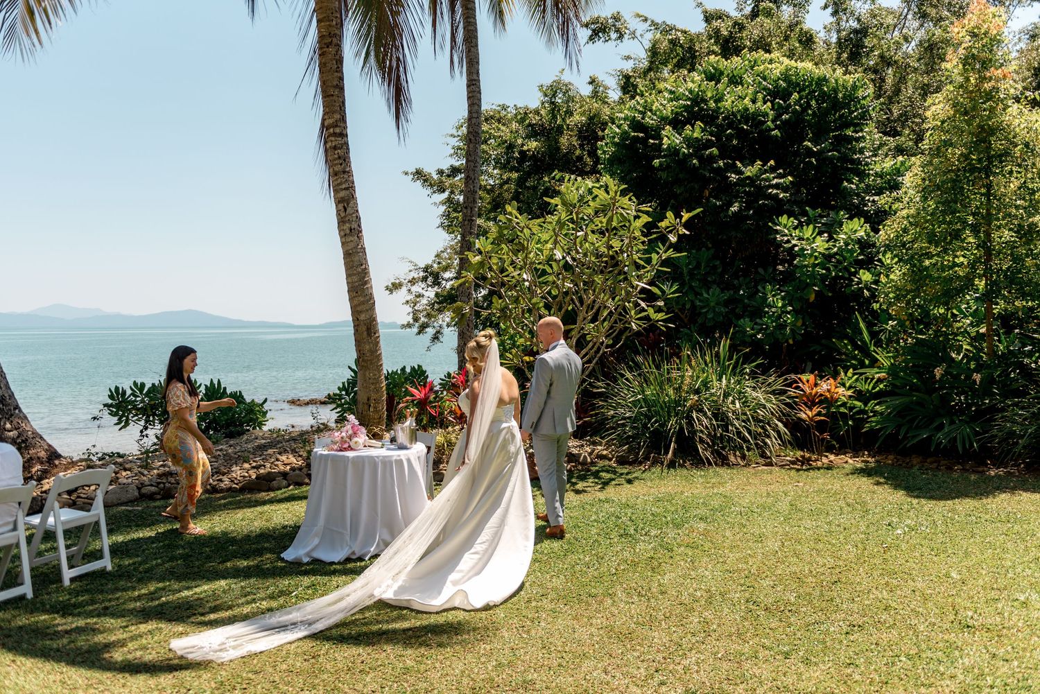Bride and groom at cake table in tropical beachside garden venue.