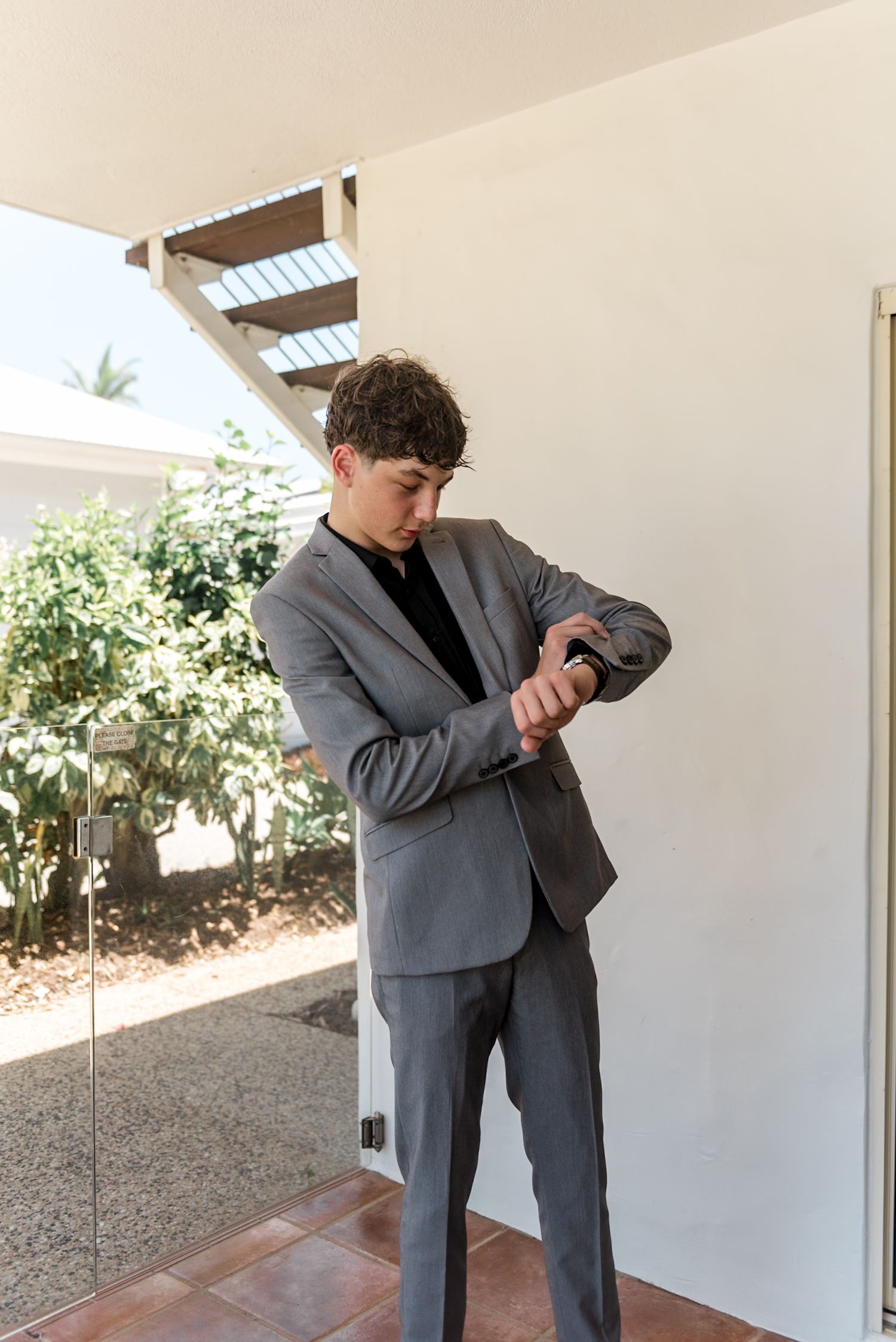 Young man in gray suit checking his watch while standing outdoors.
