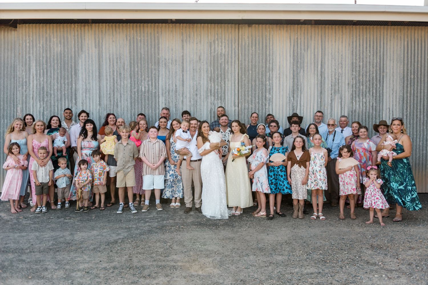 Large wedding group portrait of bride, groom, family and guests posing outside a rustic barn.