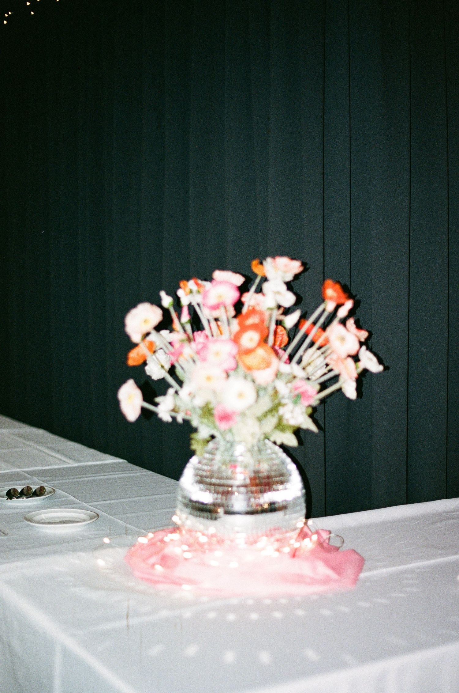 Colorful floral centerpiece in disco ball vase on white tablecloth at wedding reception.