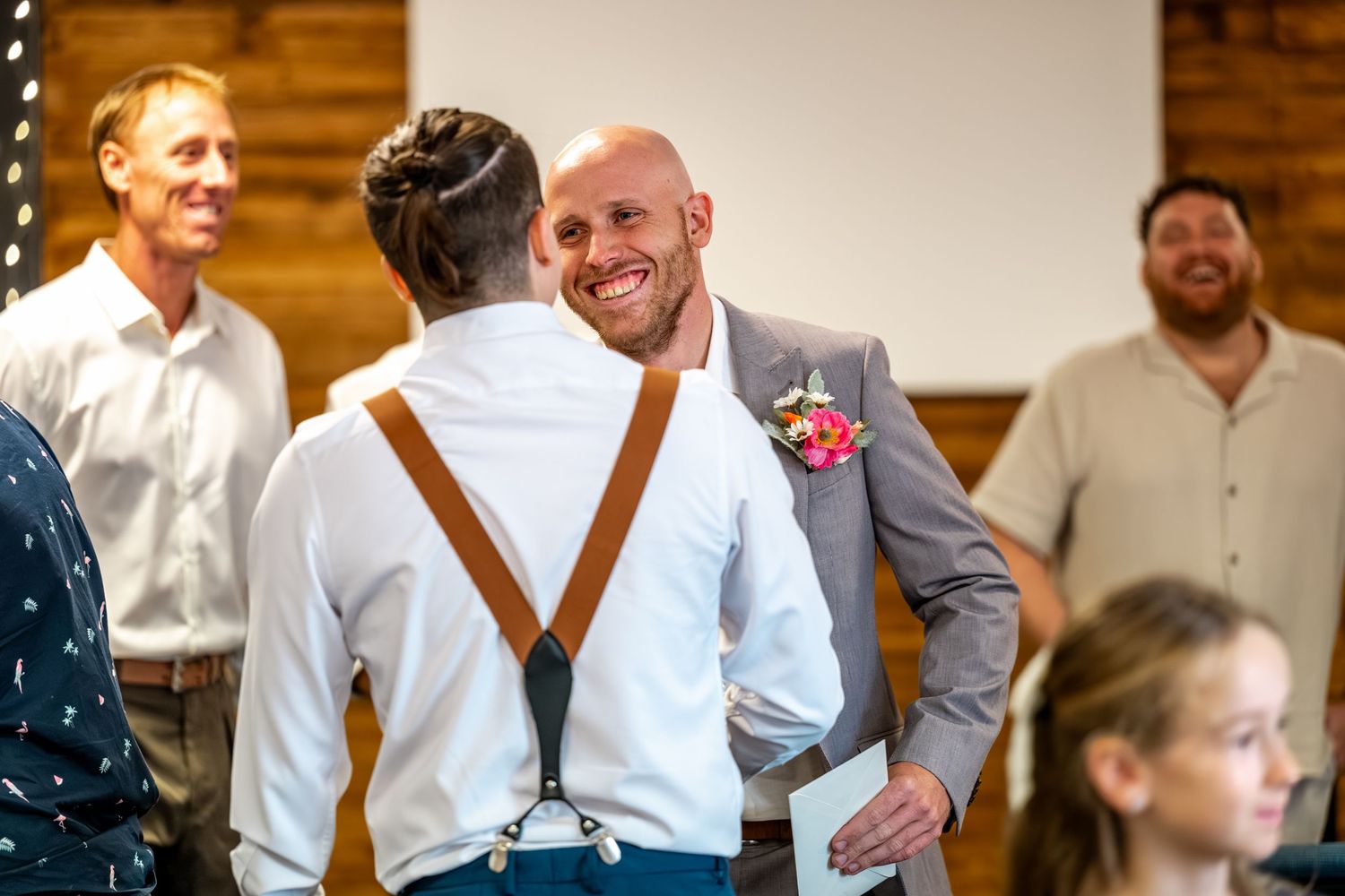 Smiling groom in grey suit with boutonniere greeting guests at wedding venue.