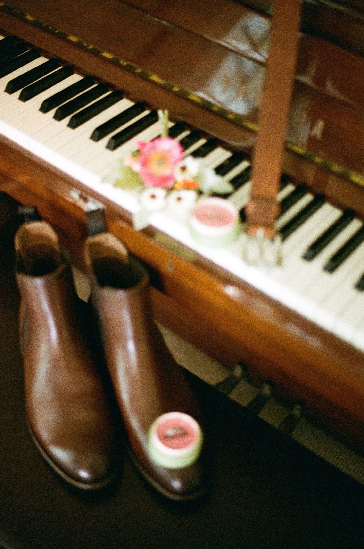 Brown leather Chelsea boots and wedding ring box displayed on vintage piano with flowers and belt.