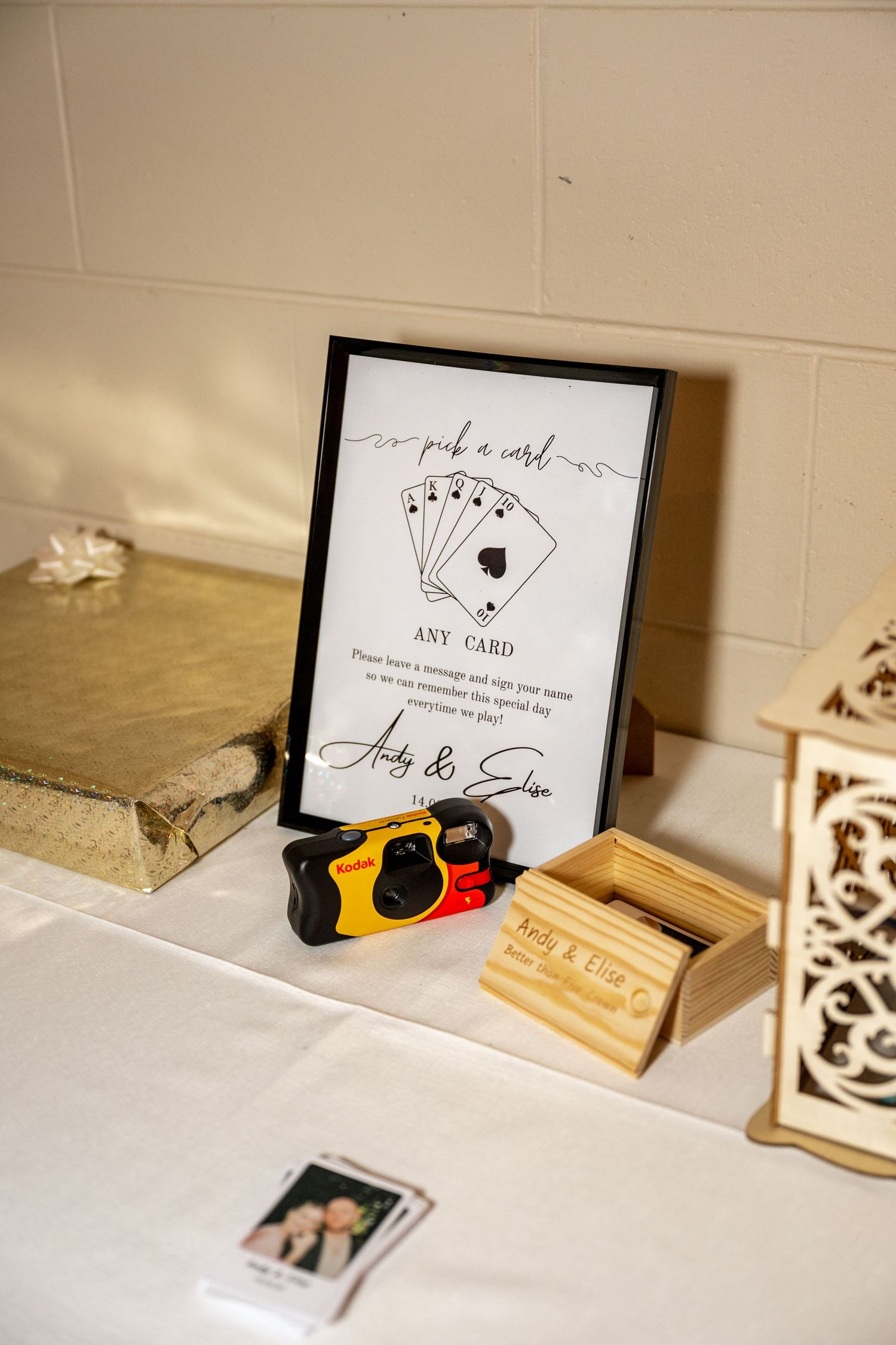 Wedding guest table featuring a Kodak disposable camera, playing card sign, and wooden keepsake box for Andy and Elise.