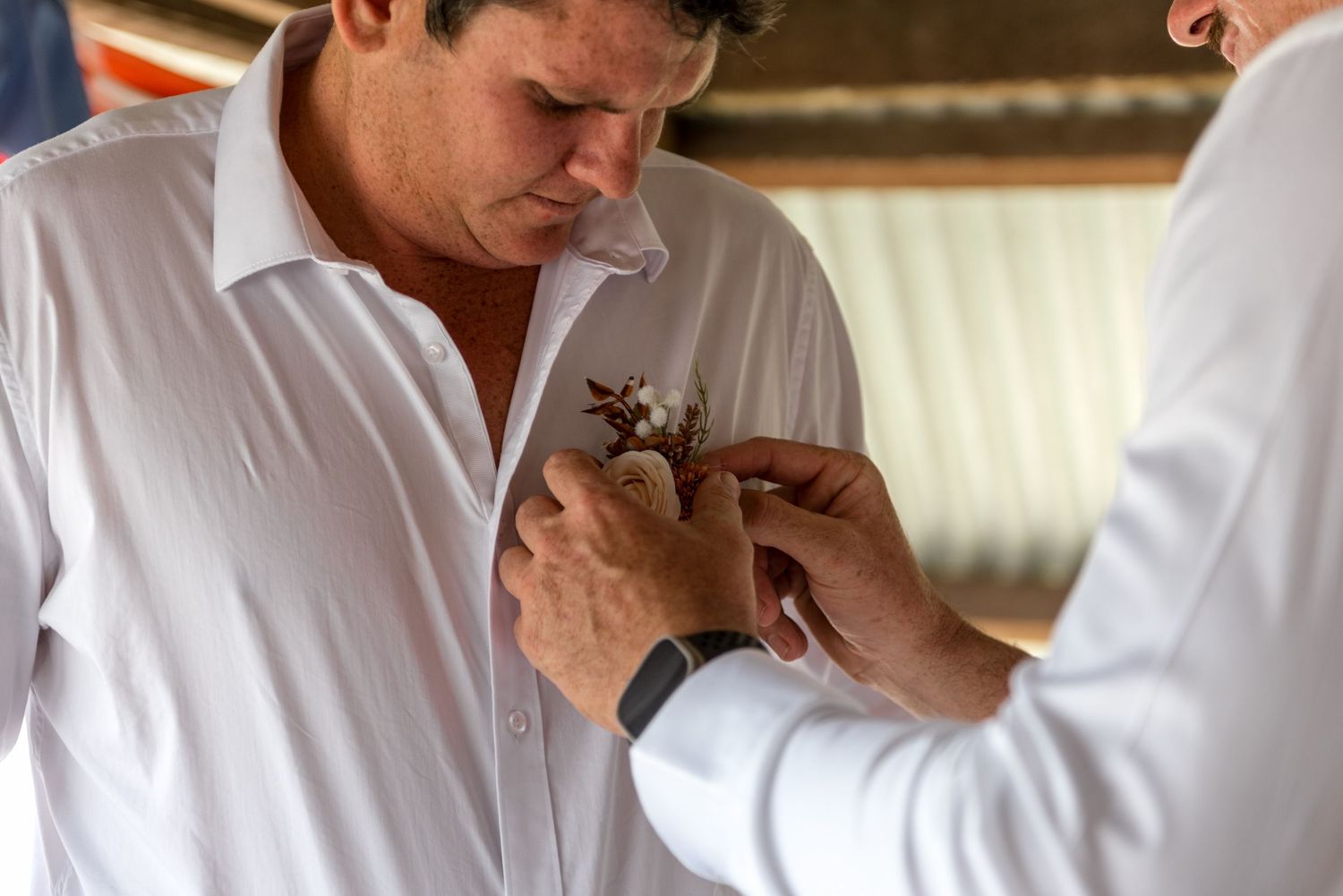 Groomsman in white shirt having a floral boutonniere pinned to his lapel before the wedding.