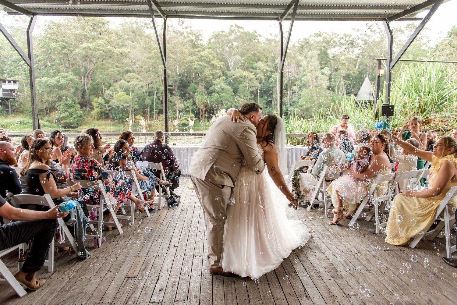Bride and groom share a romantic dip kiss at the altar during outdoor wedding ceremony with guests.