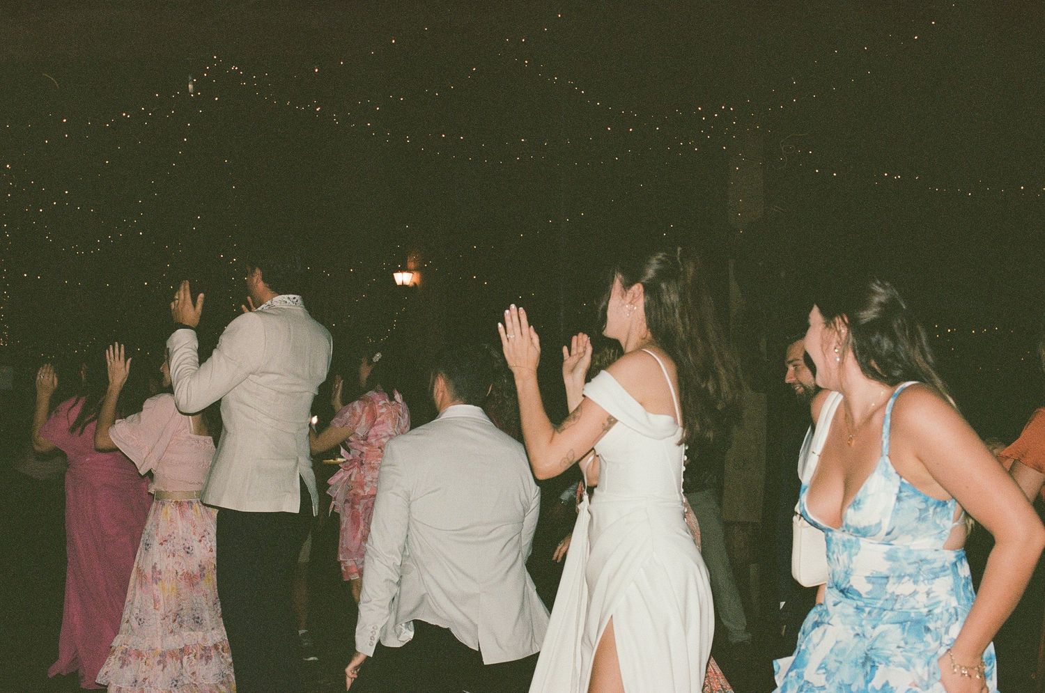 Group of guests dancing joyfully at an outdoor wedding reception under a dark evening sky.