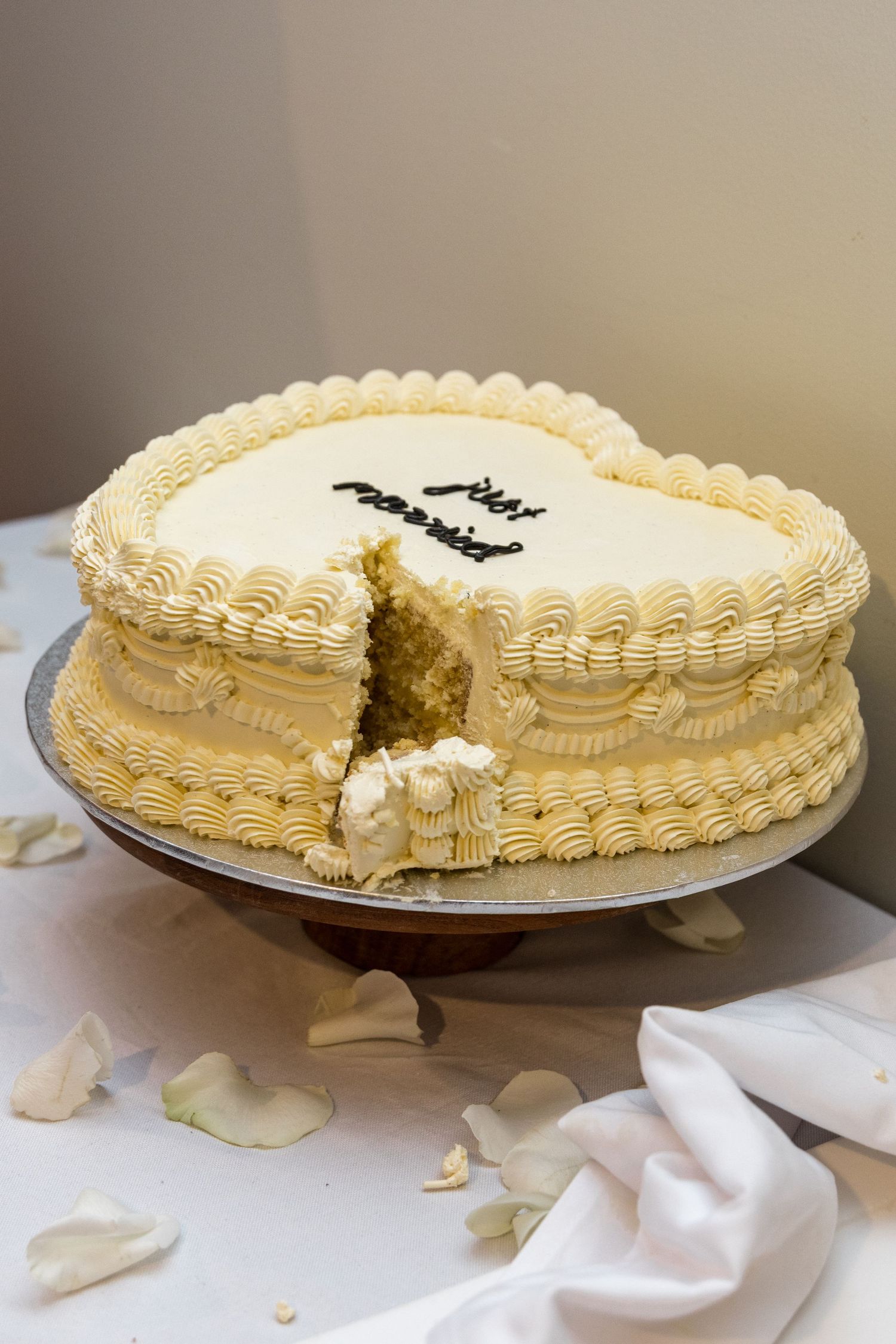 Heart-shaped just married white frosted wedding cake with a slice removed on a cake stand.