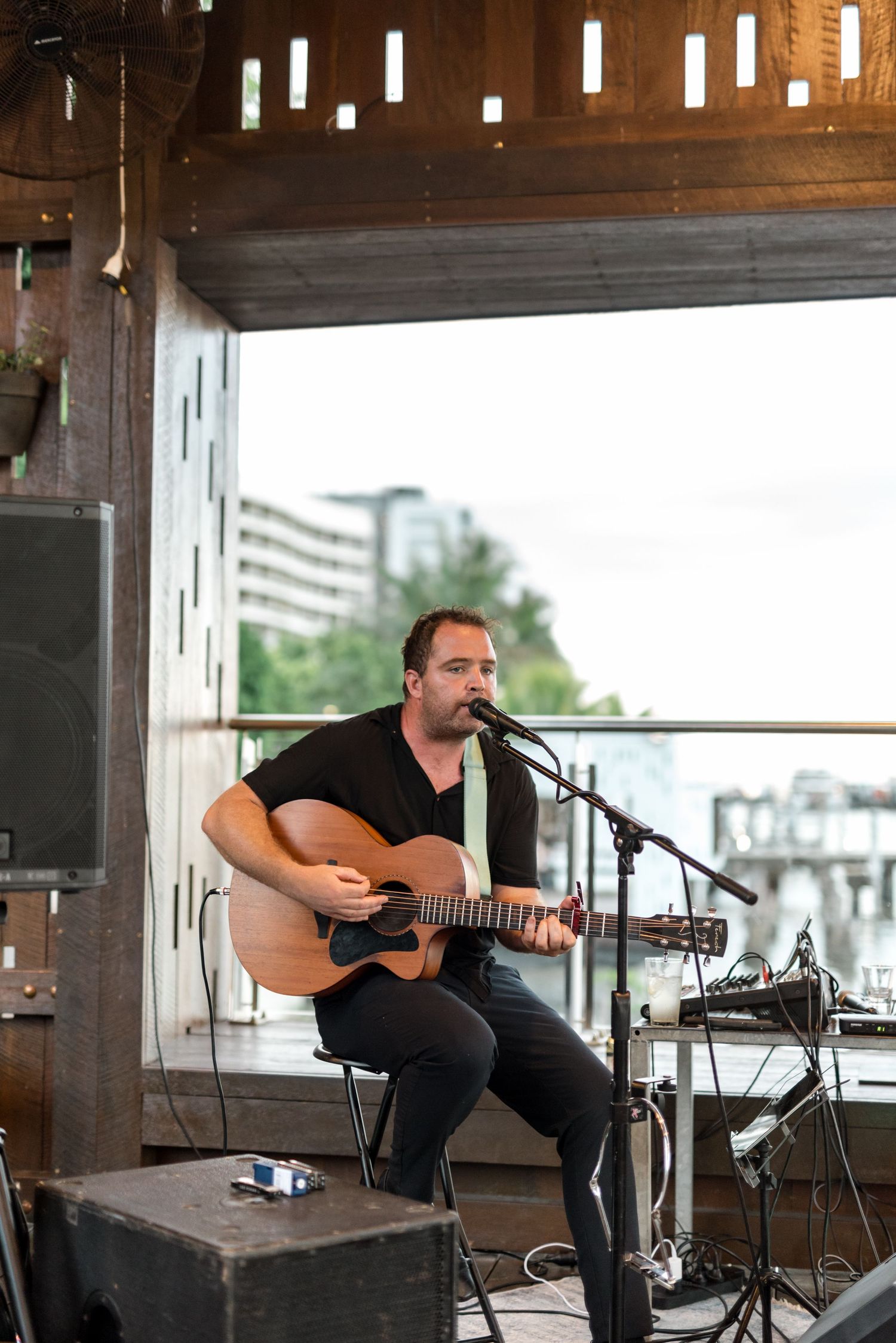 Male musician playing acoustic guitar and singing into microphone at outdoor wedding venue.