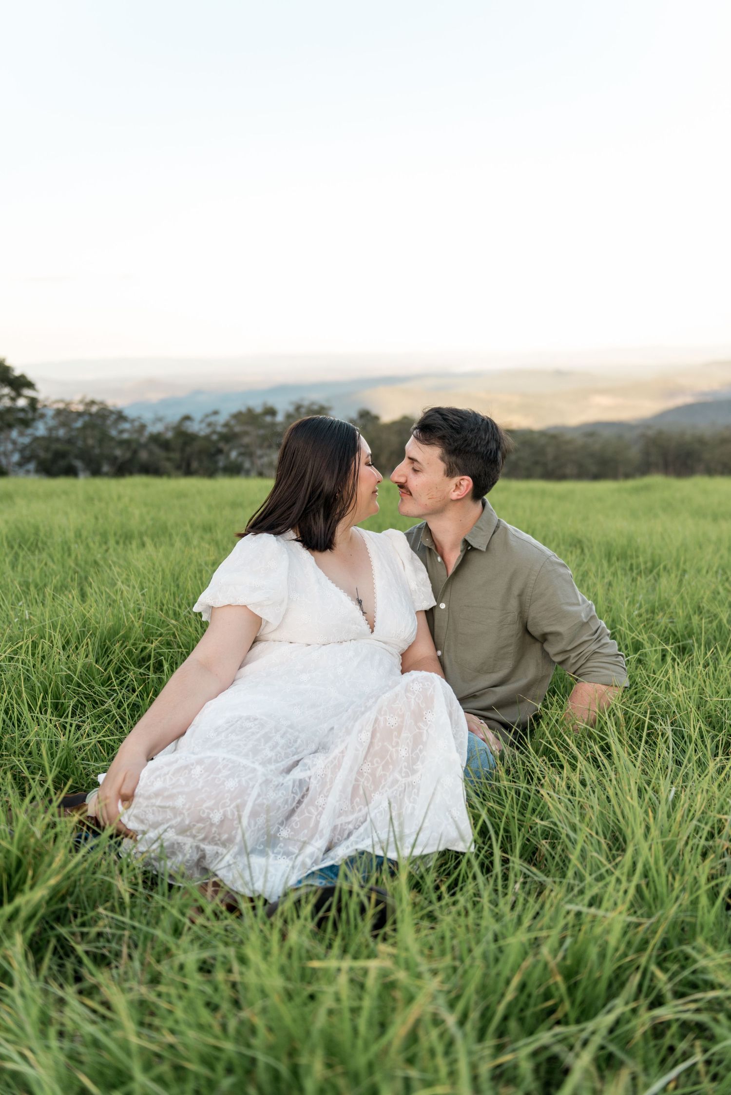 Couple sitting close together in tall green grass sharing a romantic moment.