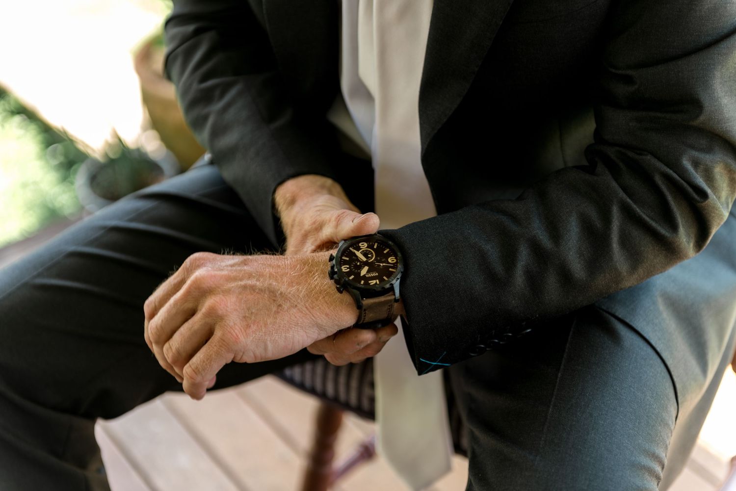 Close-up of a groom in a dark suit adjusting his luxury black watch before the wedding ceremony.