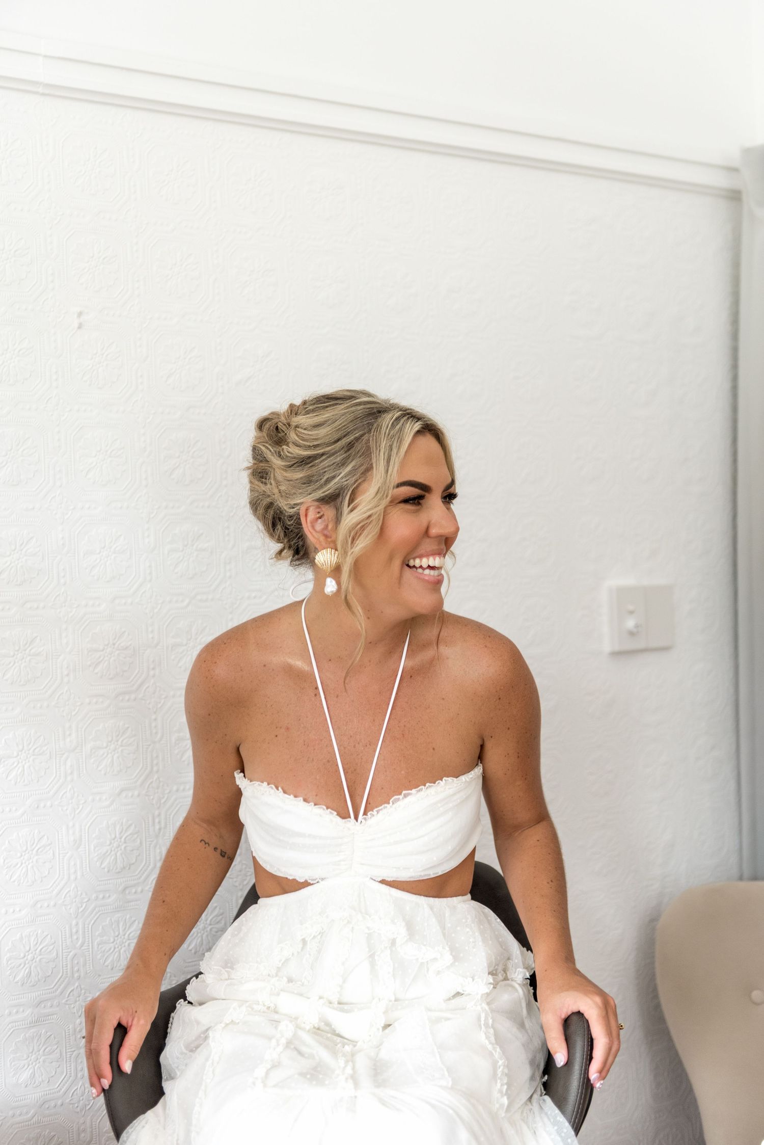 Radiant bride in white two-piece wedding dress laughing with pearl earrings.