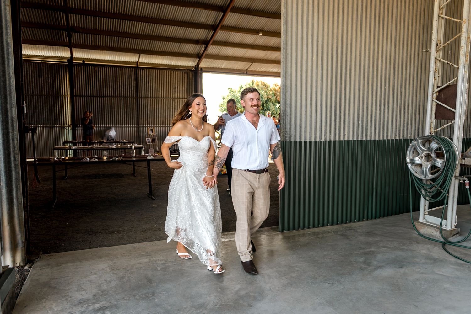 Bride in lace gown walks with groom through open barn doors at outdoor wedding.