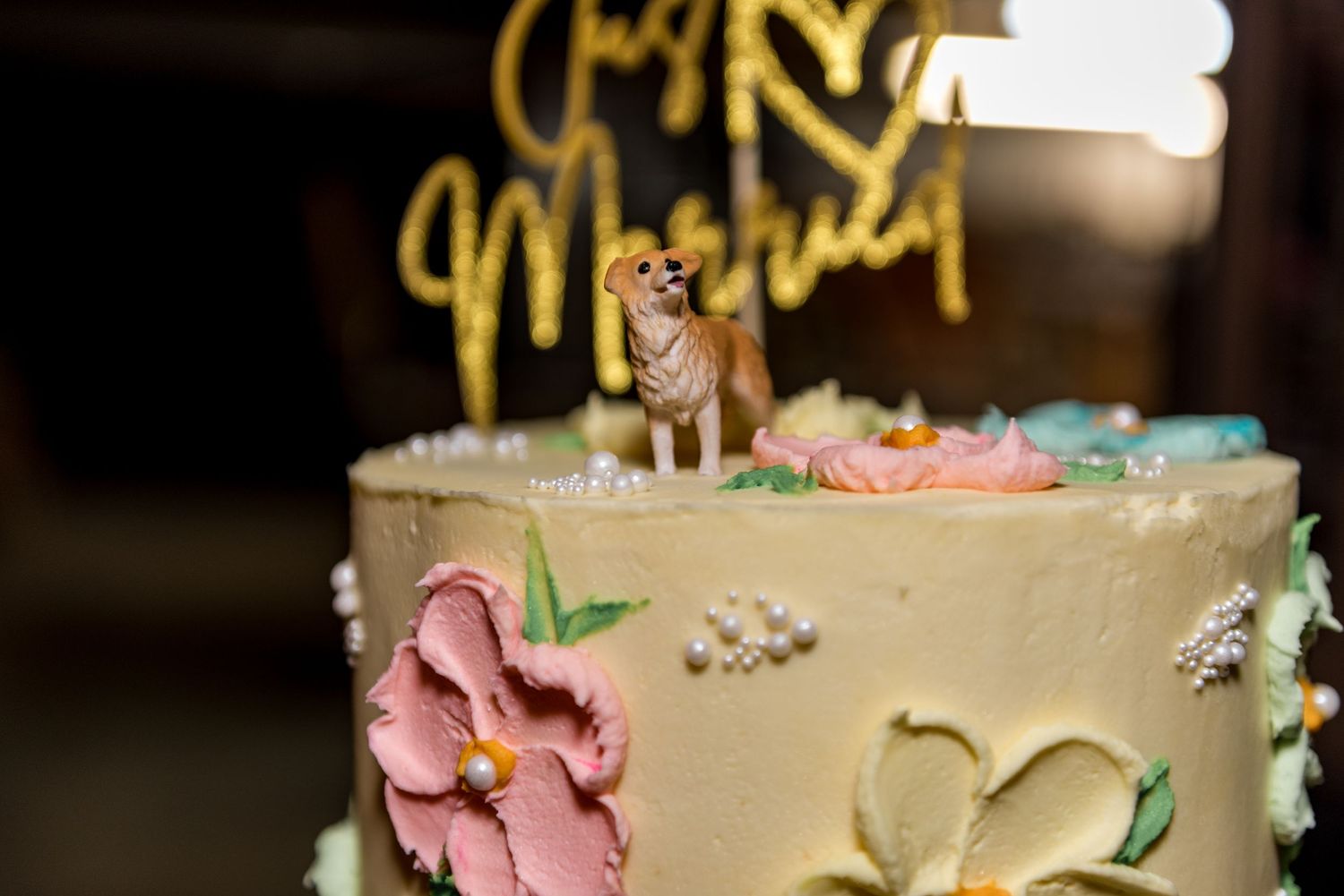 Close-up of elegant wedding cake with dog figurine topper, pink and blue flowers, and gold Just Married cake topper.