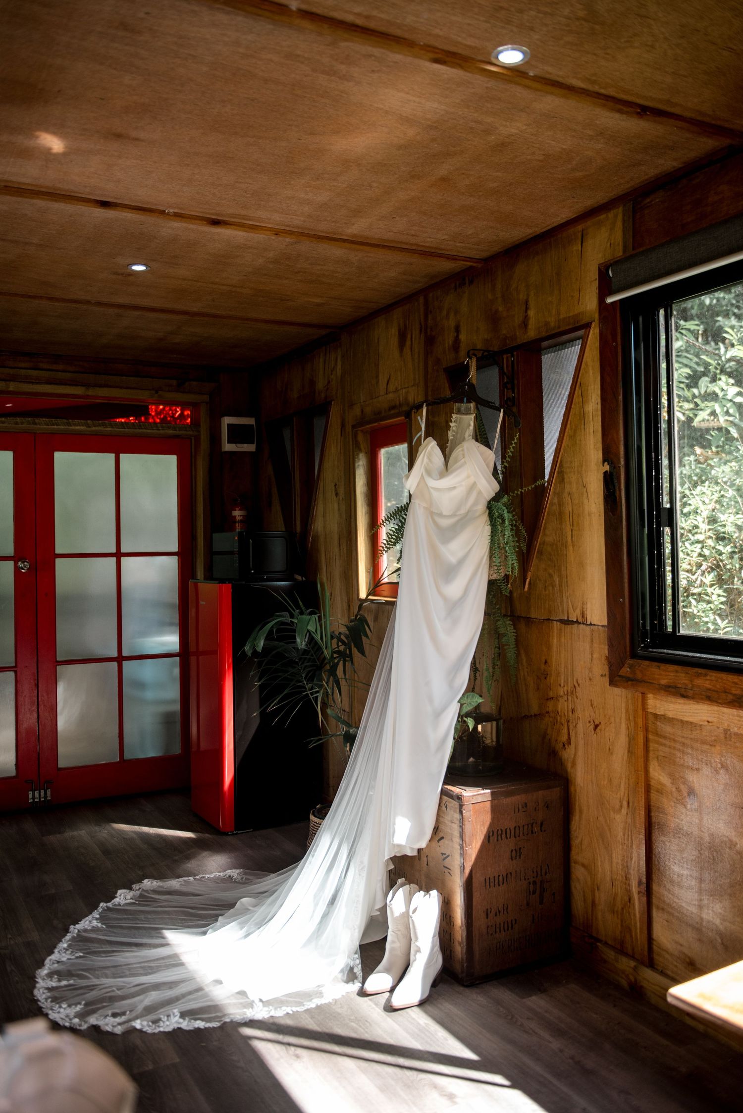 Elegant white wedding dress with long veil hanging in a rustic wooden cabin.