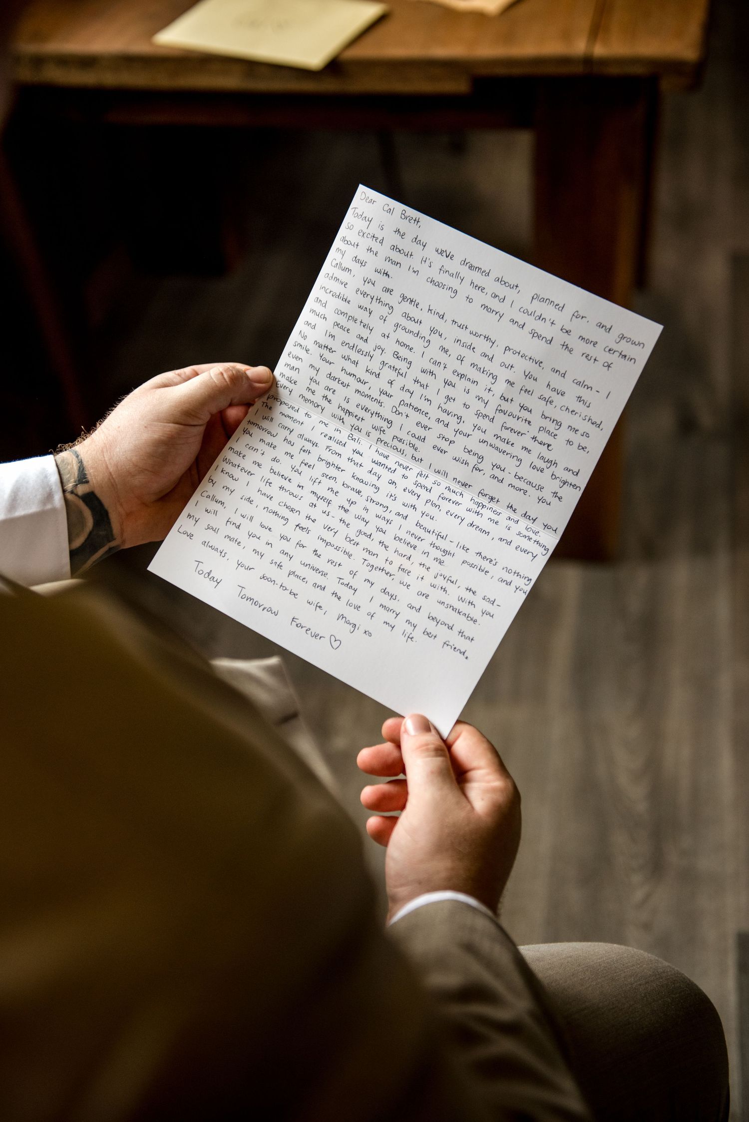 Close-up of groom reading handwritten wedding letter held in both hands before ceremony.