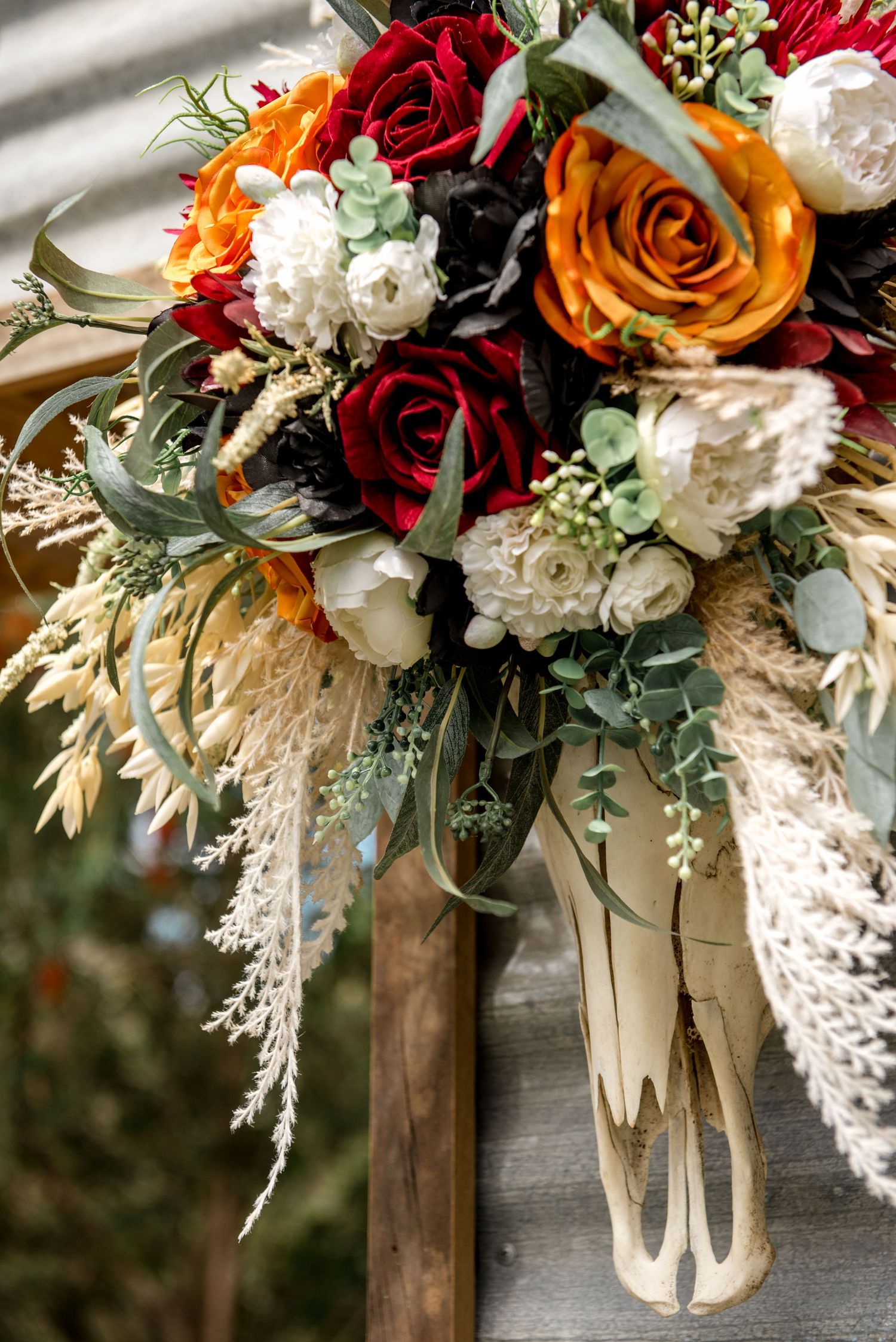 Lush bridal bouquet featuring red, orange, and white roses with pampas grass and eucalyptus greenery accents.
